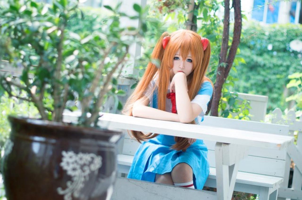 侒君扮演明日香坐在白色长椅上，趴着桌子凝望镜头