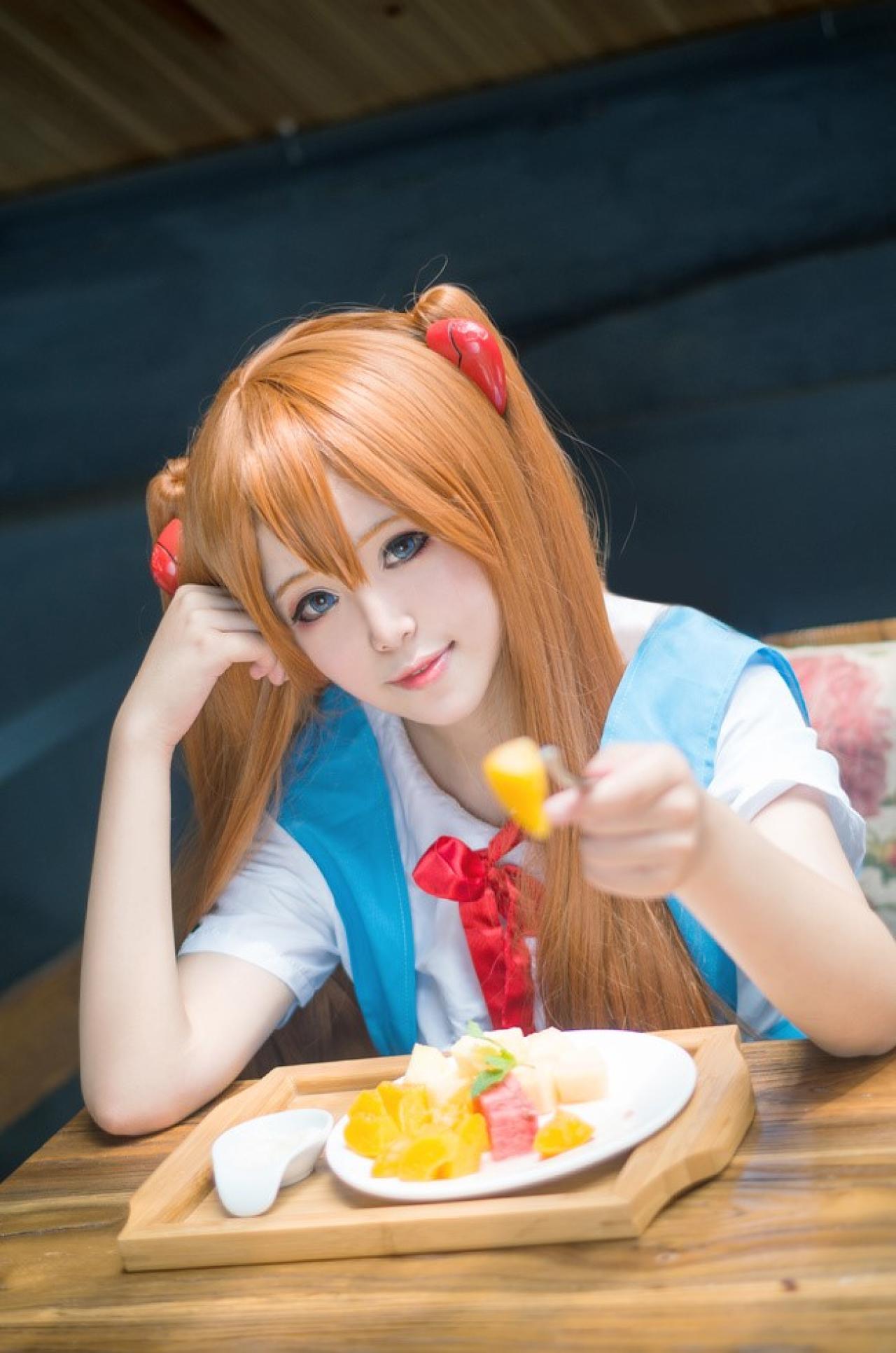 侒君扮演明日香右手撑着头，左手用叉子叉起一片水果