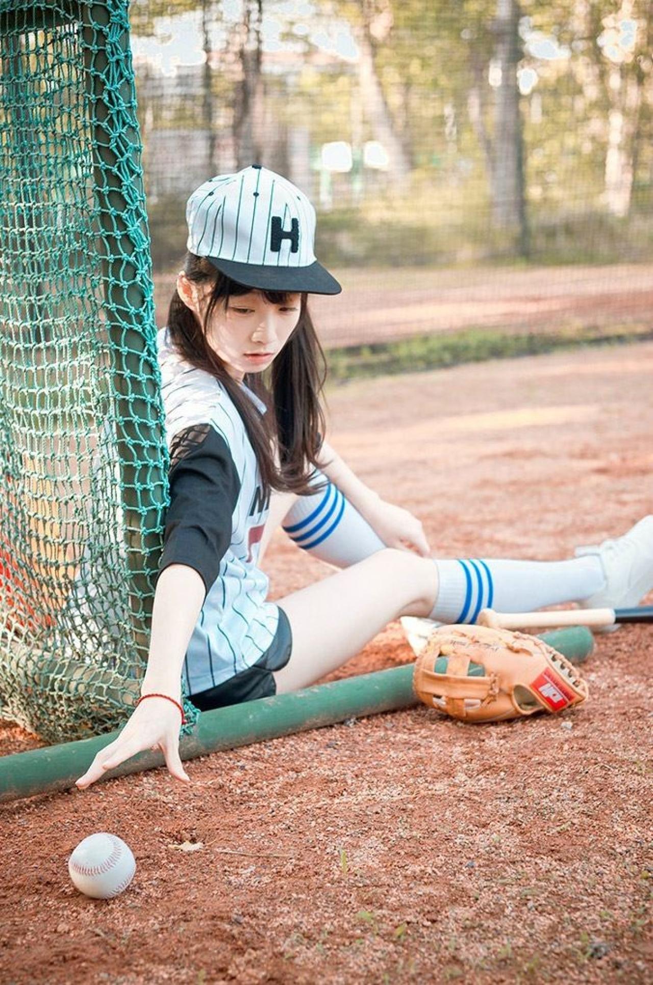 馋宝宝靠在棒球网上，低头伸出右手去拿棒球