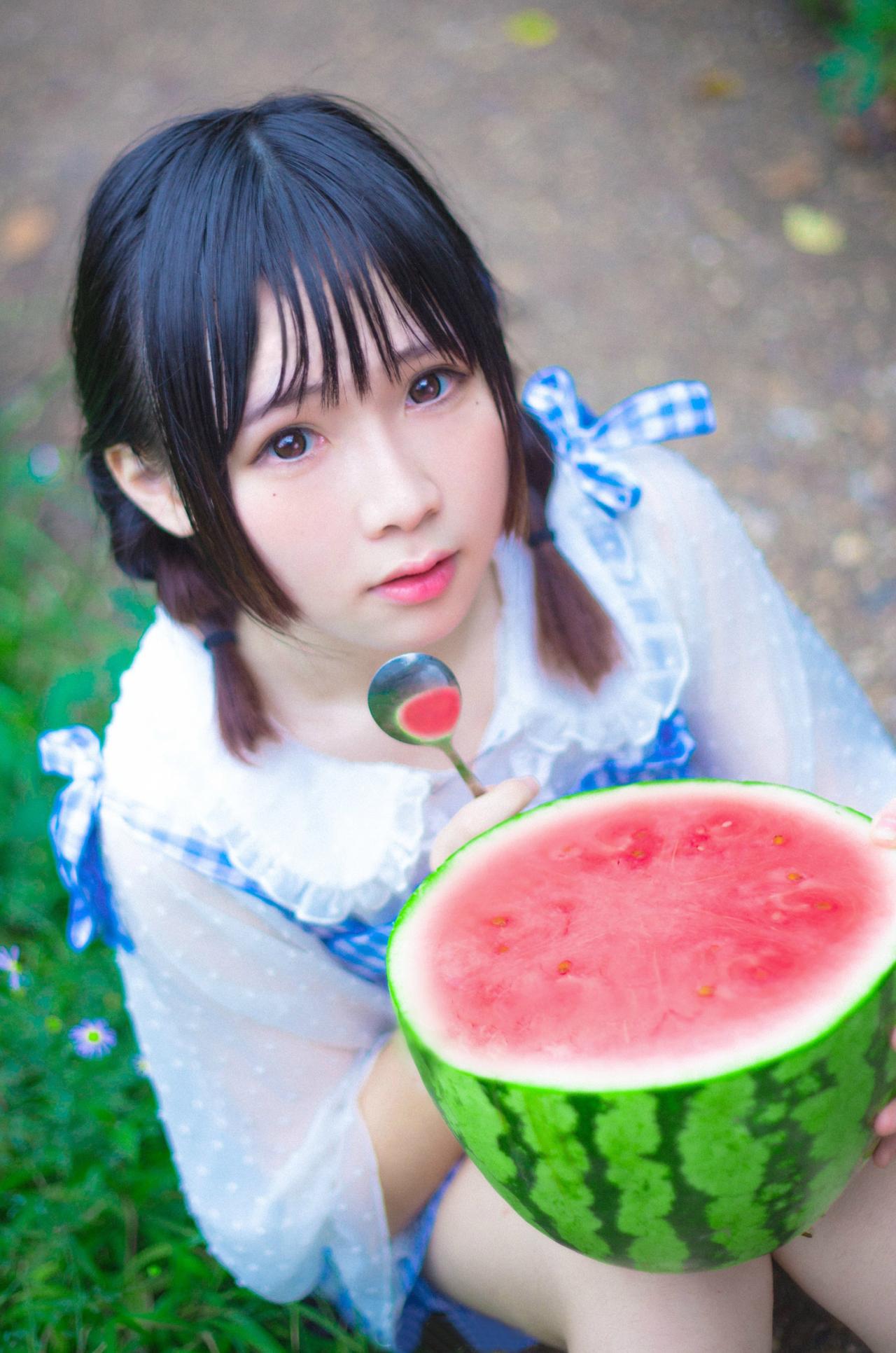 九樱喵坐在草地上，膝盖上枕着半个大西瓜，左手扶着西瓜，右手握着小勺子的姿势