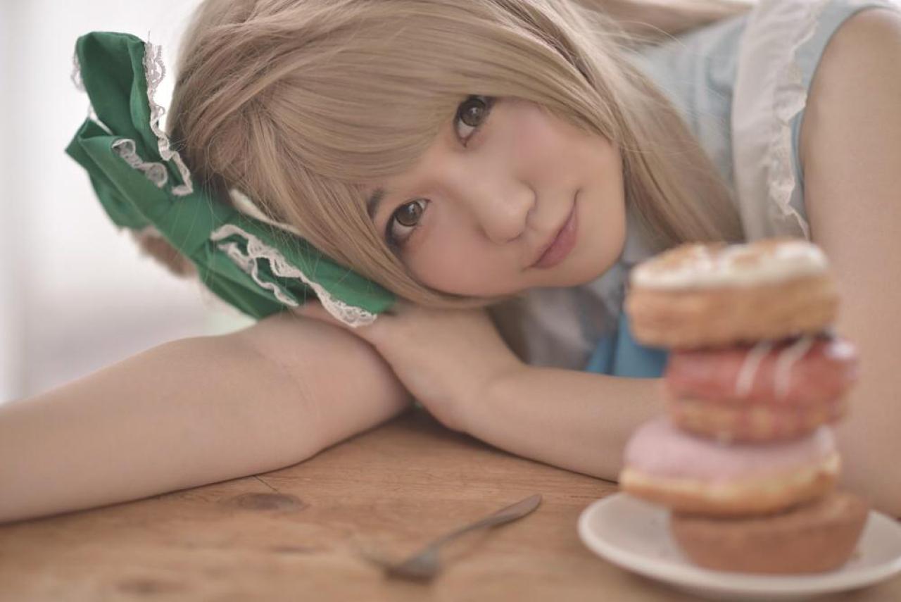 橘猫汰扮演南小鸟右手伸直，头靠在上面，左手放在右手上，扒在餐桌上的歪着头看镜头的姿势。眼前的餐桌上放着一叠面包圈。