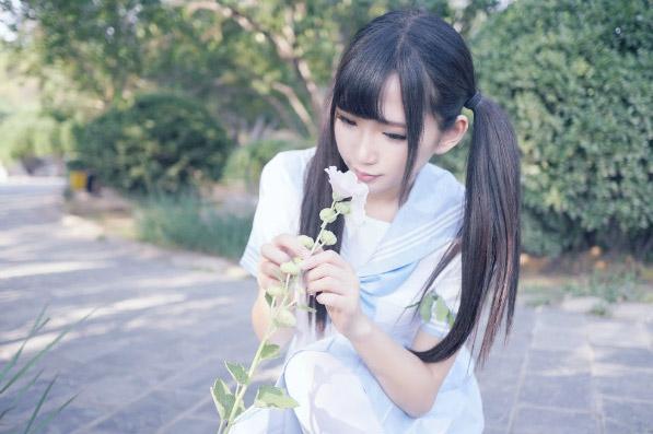 姗酱蹲在路边，双手扶着花茎，凑到花朵前，用心嗅花的姿势