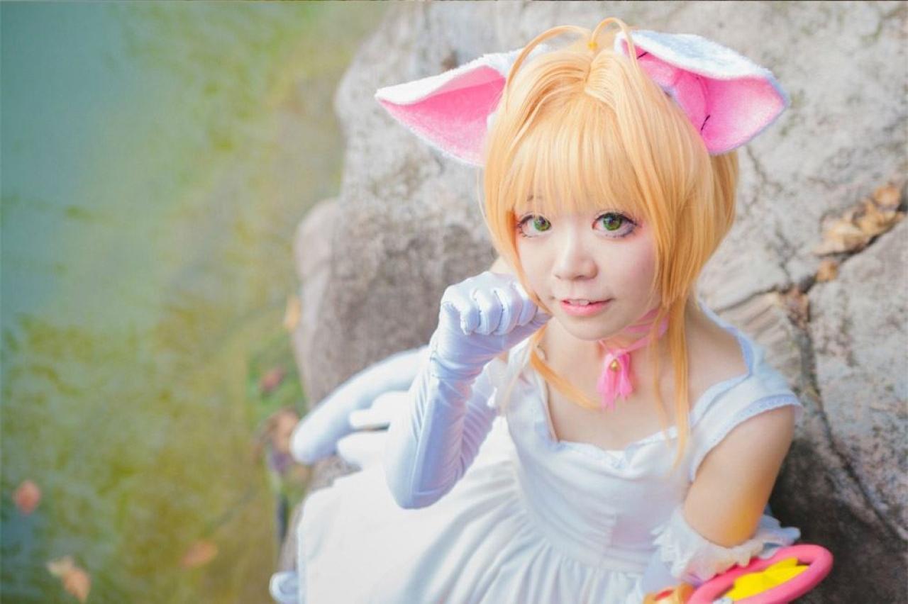 阿八扮演木之本樱坐在水边，左手拿着魔法杖，右手作小猫手势