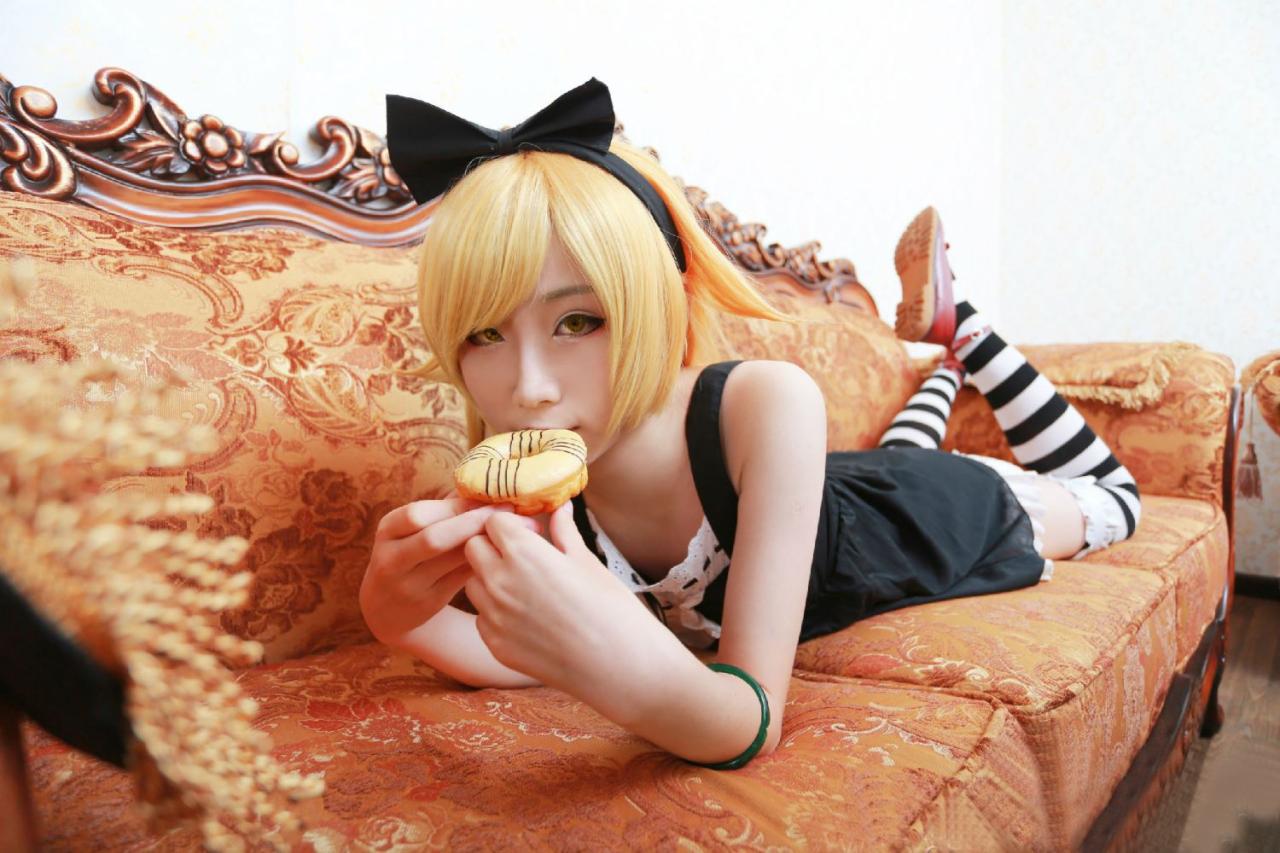 下北原喵扮演忍野忍扒在沙发上，双手正把一个甜甜圈往嘴里送