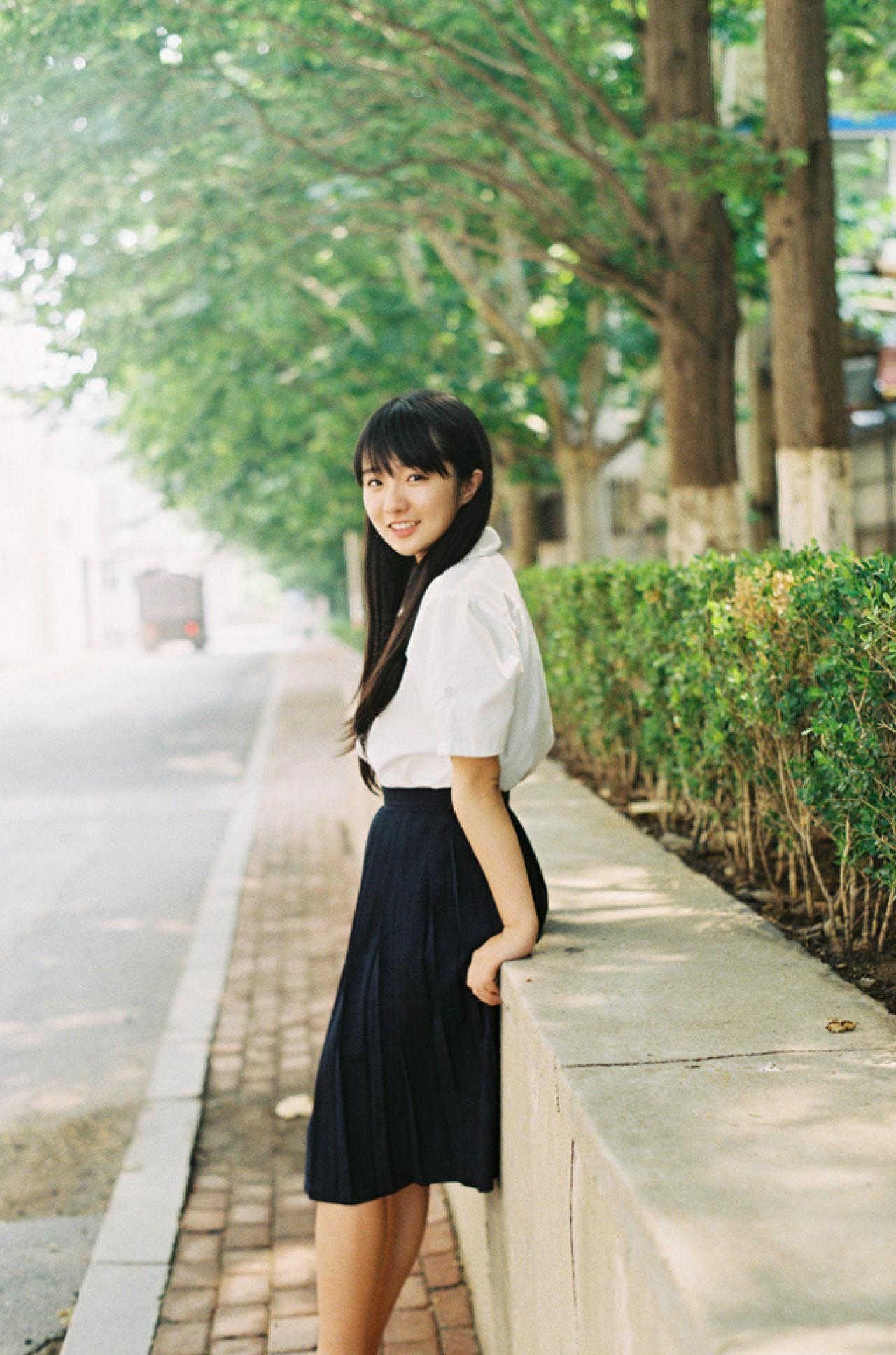 小陆离靠在花池的矮墙上侧面照，背景是一直延伸的马路