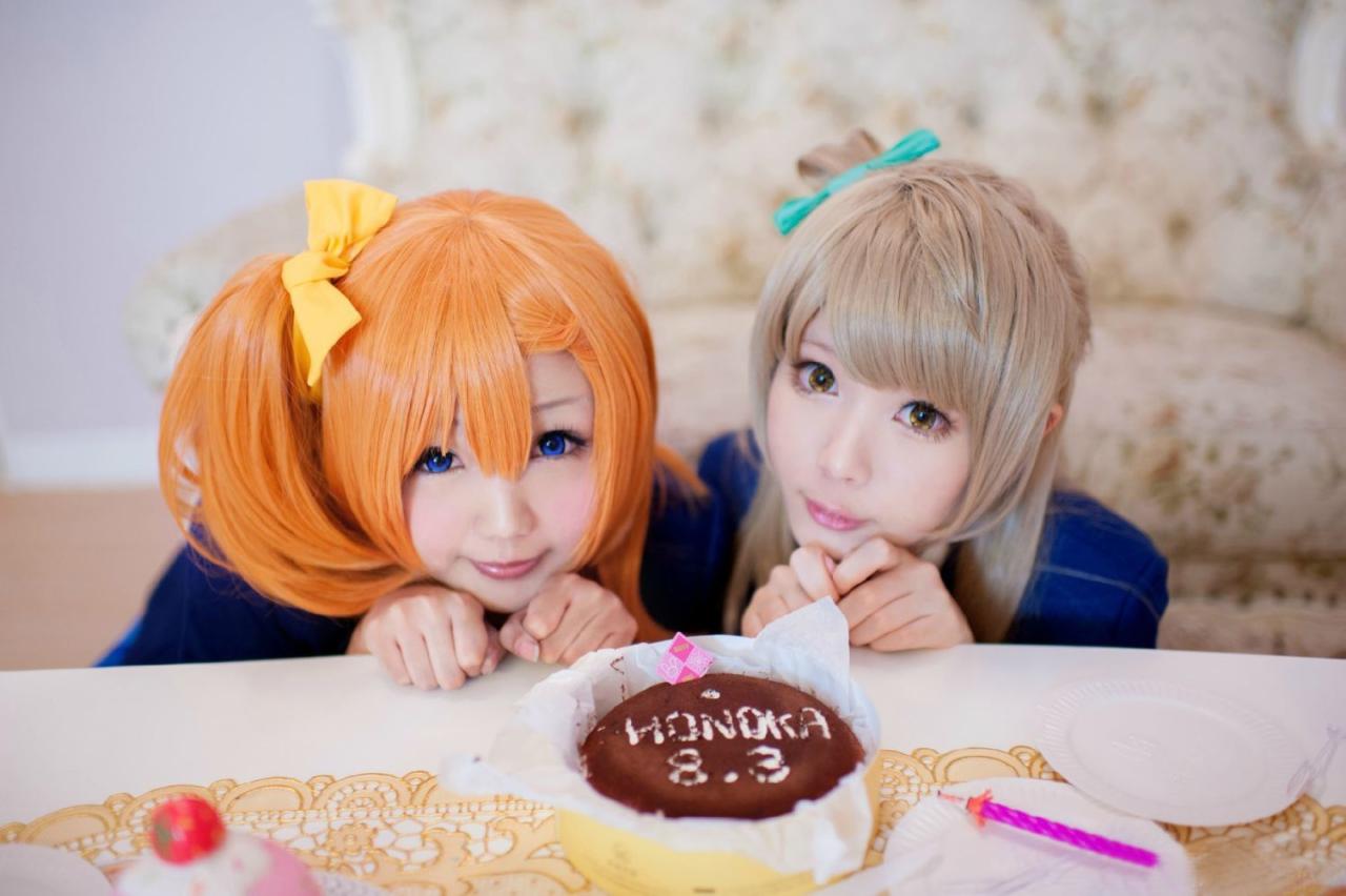 肉感少女Neneko扮演高坂穗乃果和霜月扮演南小鸟蹲在餐桌旁，扮成小猫卖萌，餐桌上摆着生日蛋糕，蛋糕上写着HONOKA 8.3