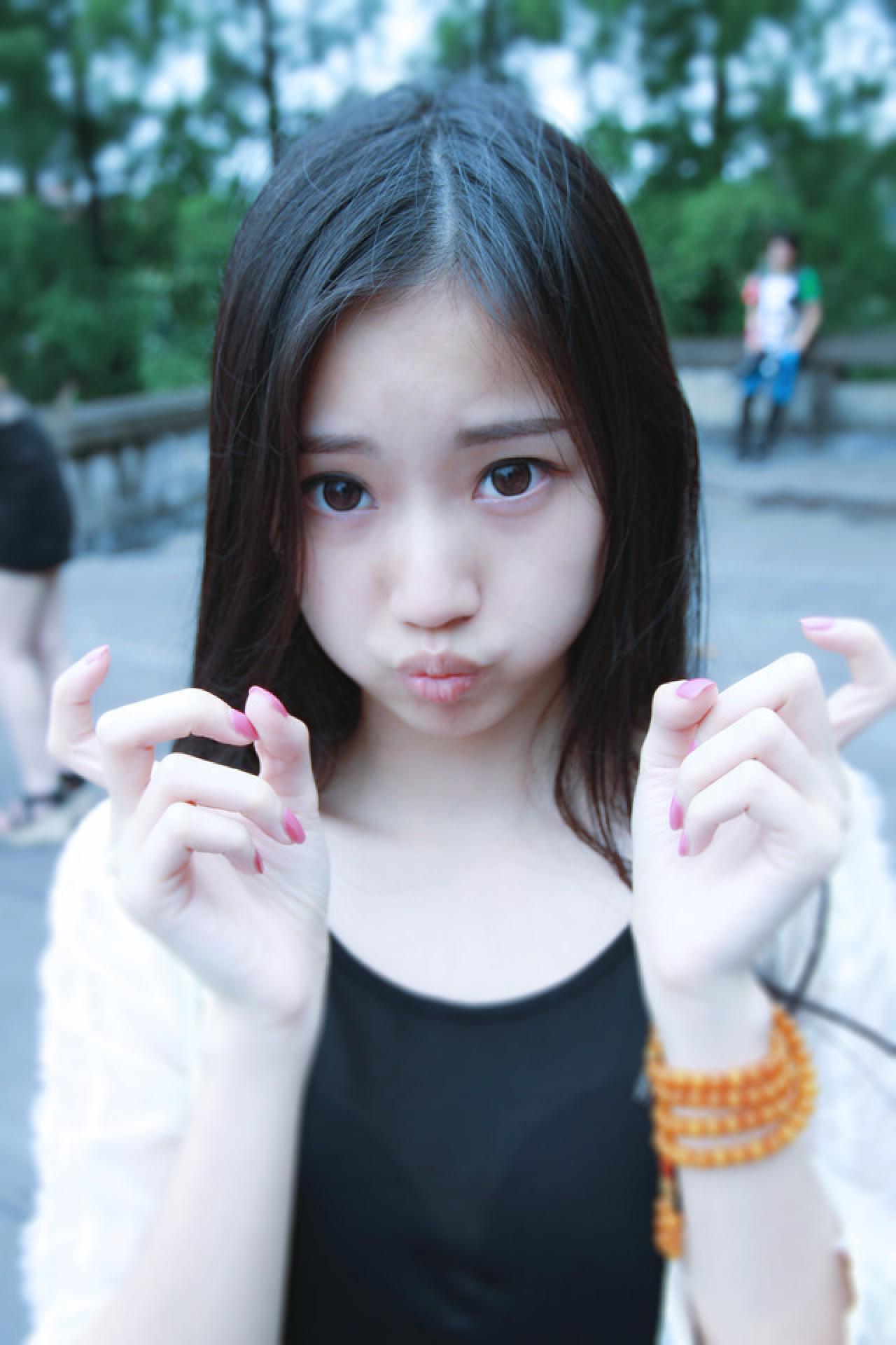 黑长直萌妹子双手放在脸颊两侧，勾手指嘟嘴卖萌