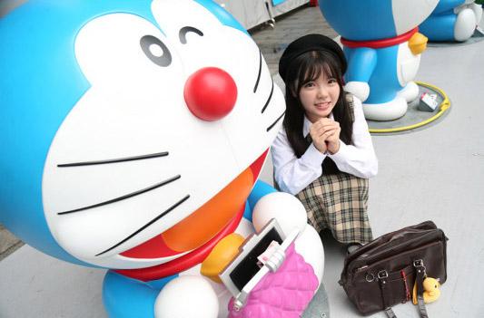 彩虹姐姐双手抱拳蹲在拿着粉色包包的哆啦A梦身旁