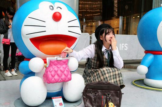 彩虹姐姐手遮住嘴，偷笑着给眨眼睛的哆啦A梦钱包里塞了100元