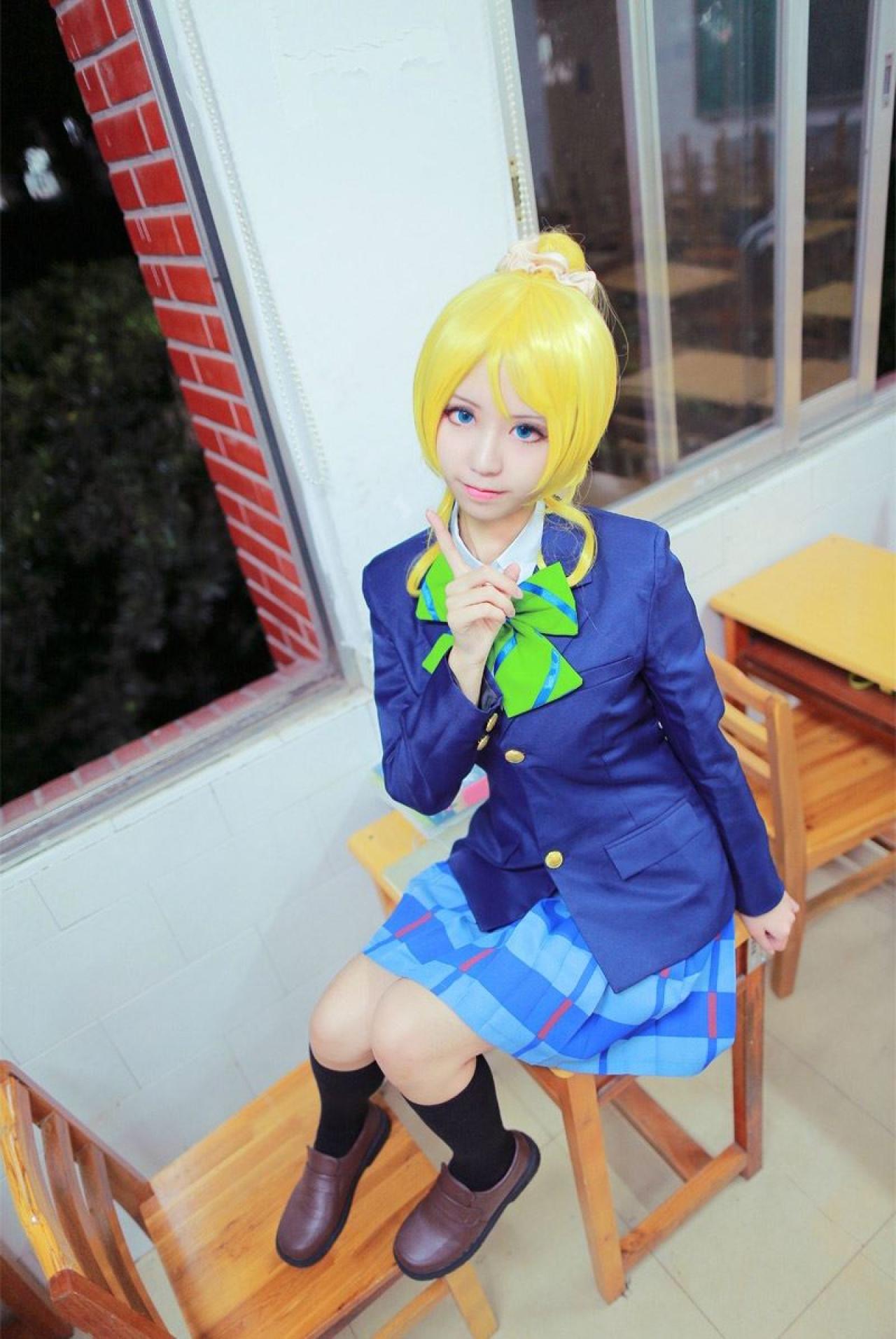 赤澤Aki扮演绚濑绘坐在桌子上，竖起食指