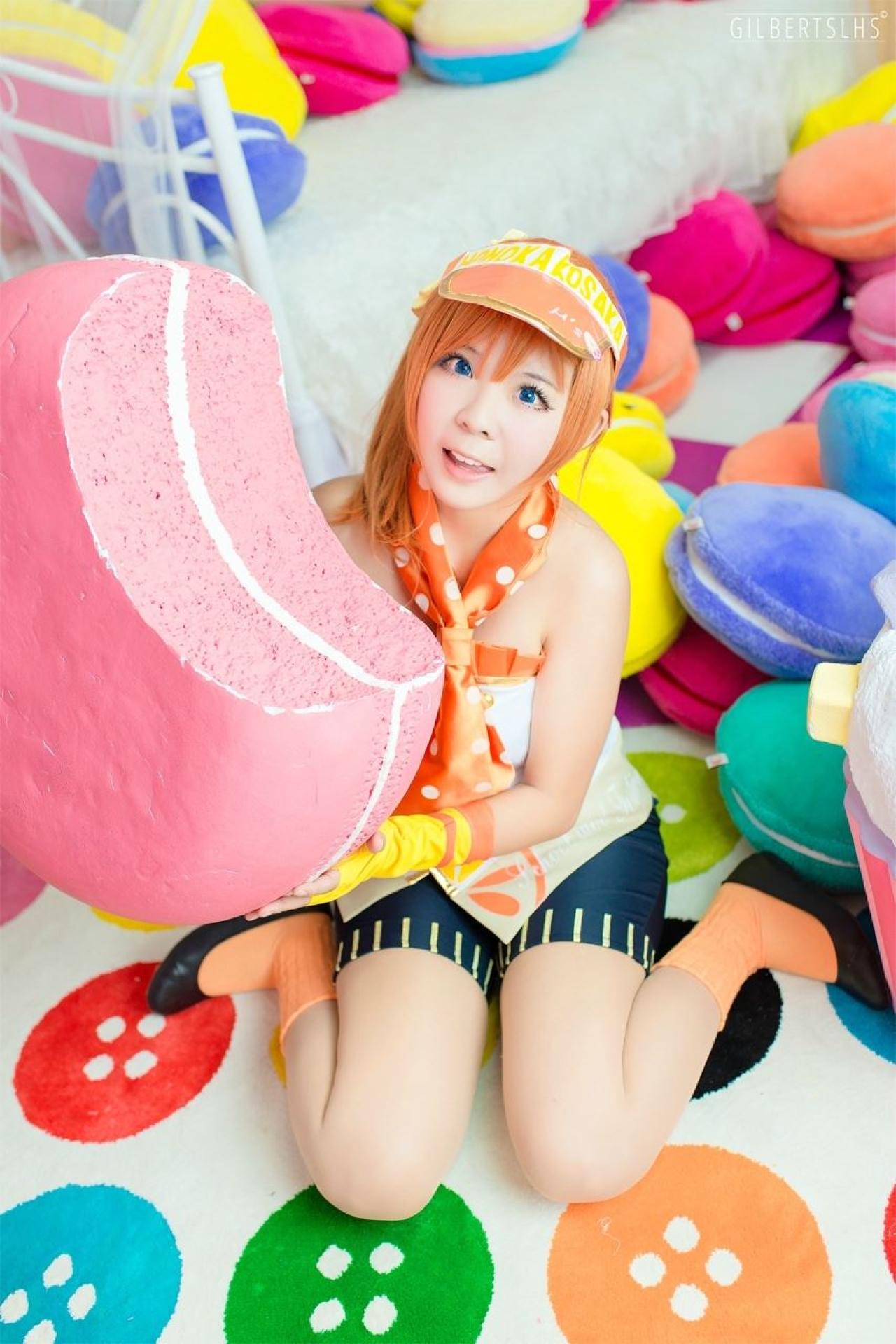 Candi糖糖扮演高坂穗乃果穿着黄白打歌服，蹲在粉色甜点身后：很美味的神情