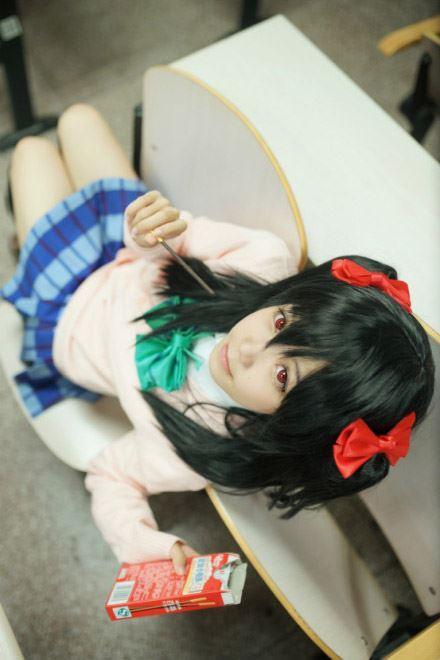 阿琴扮演矢泽妮可侧身坐在椅子上，右手捏着铅笔，左手拿着笔盒