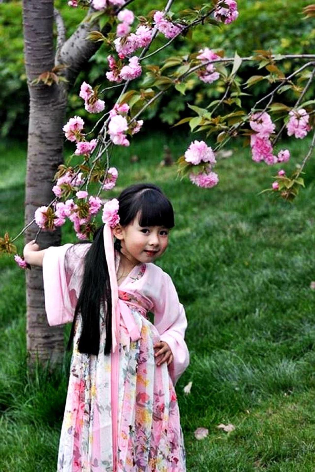 果果右手拽着樱花树枝，左手叉腰摆起了POSE（姿势）
