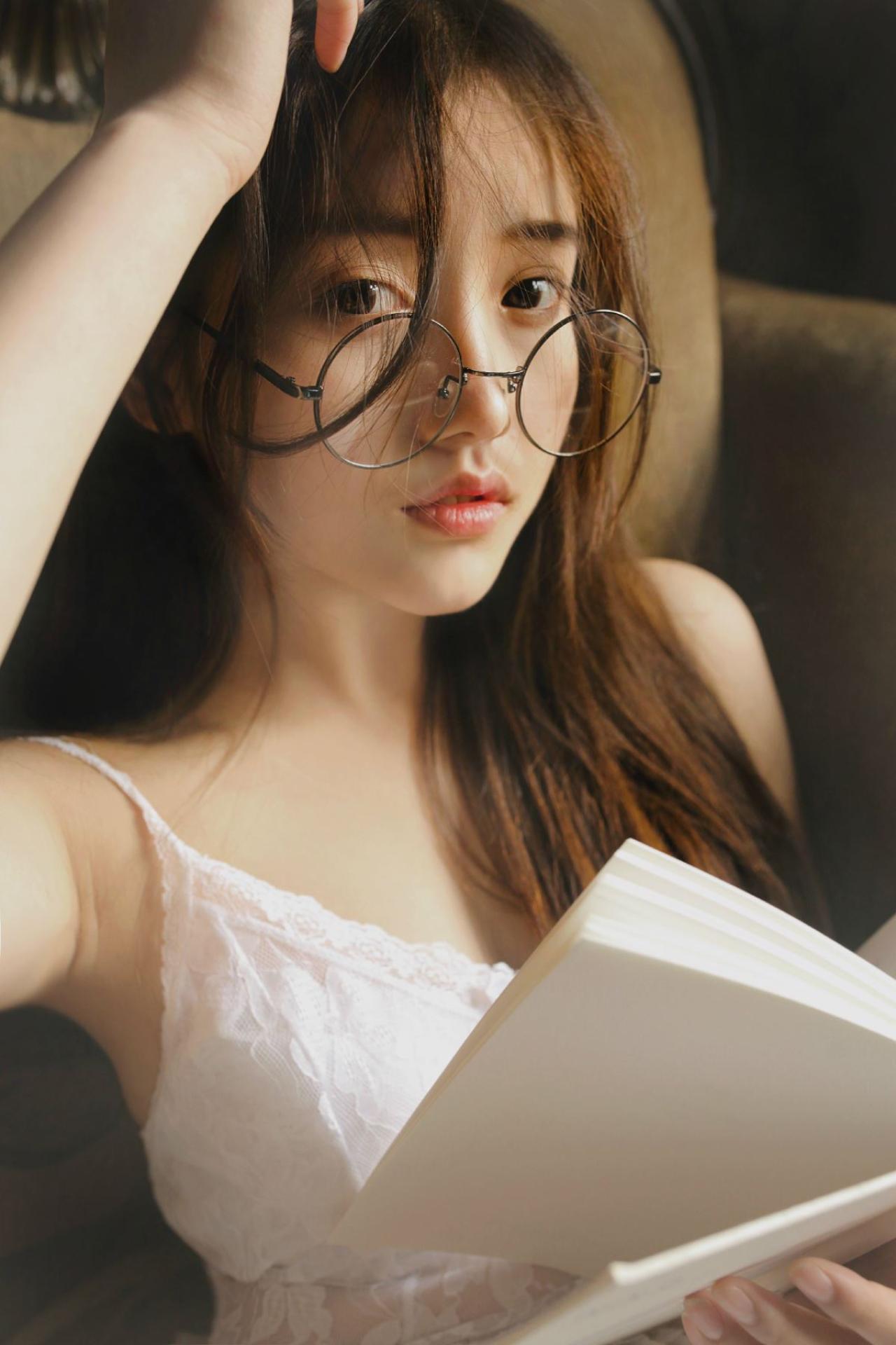 垚昕穿着白色连衣裙戴着圆框眼睛，左手轻抚头发，拿着翻开的白色书本