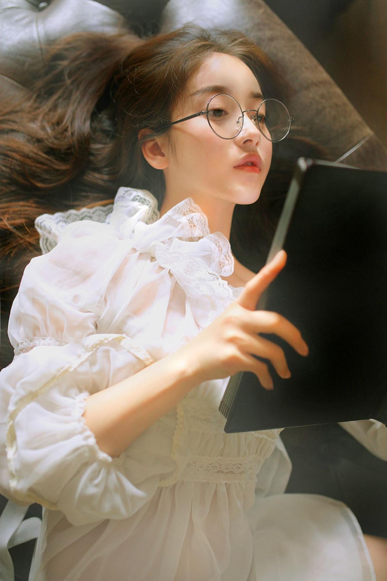 垚昕双手端着黑色课本，躺着戴着眼睛认真看着