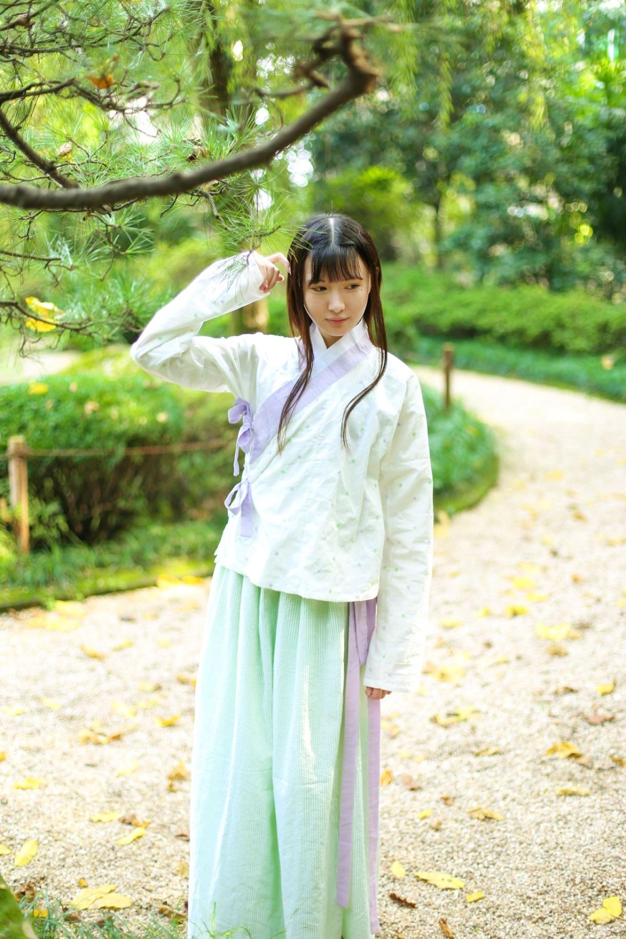 瞬瞬穿着白色上衫，绿色长裙站在松树下