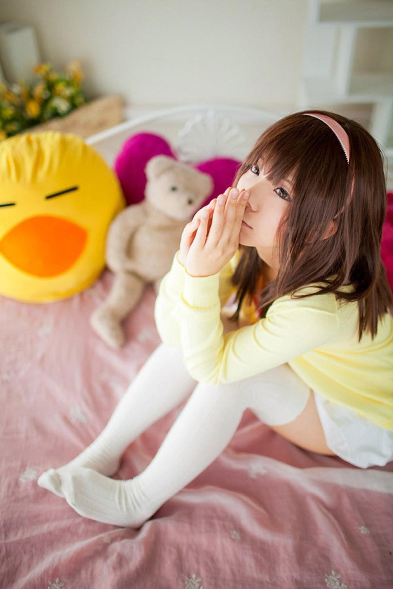 Yun Kousaka扮演千石抚子坐在床上，双臂枕在膝盖上，双手合十放在鼻尖