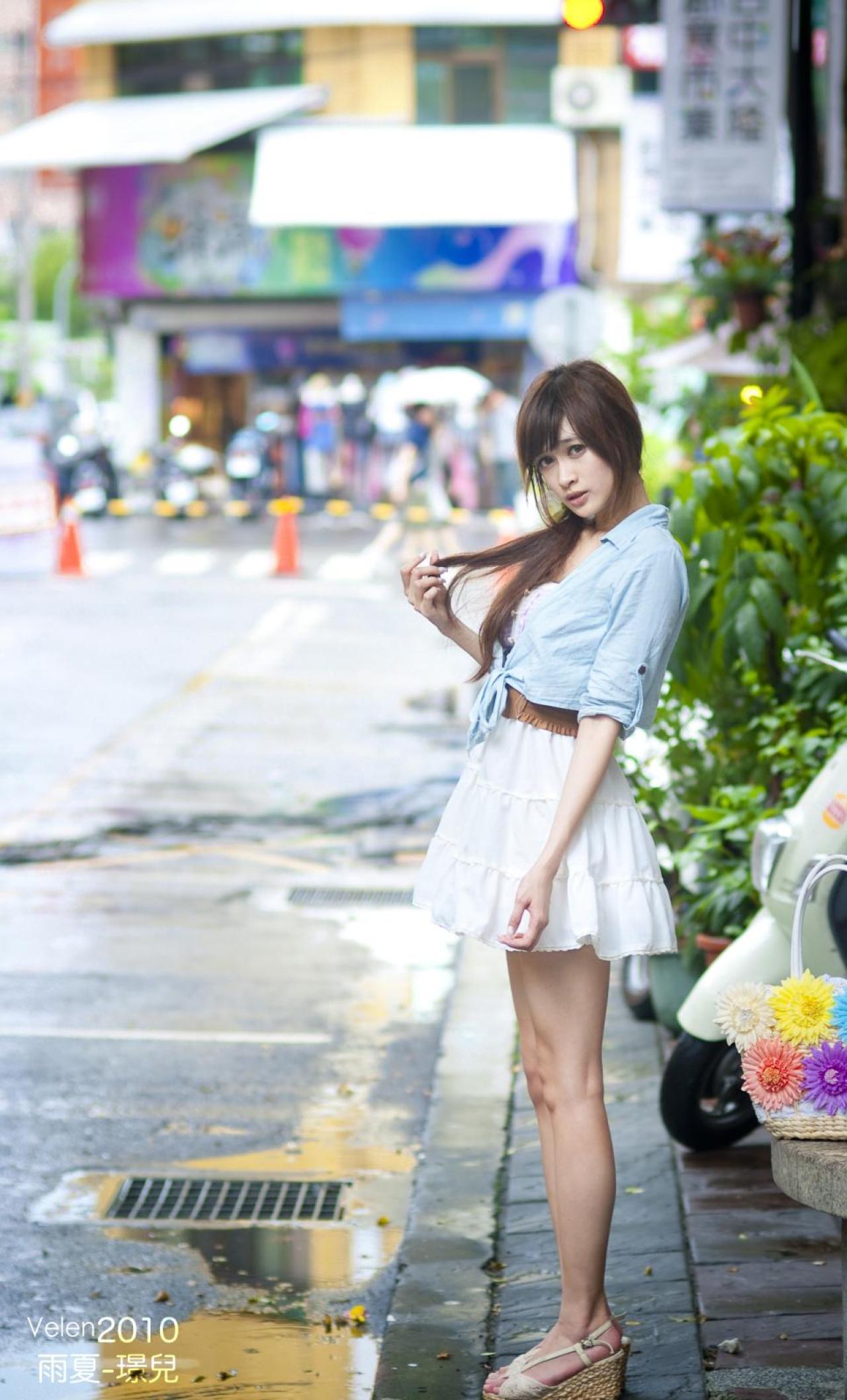 璟儿站在街角，轻抚马尾，背景是精明一街的街道和店铺