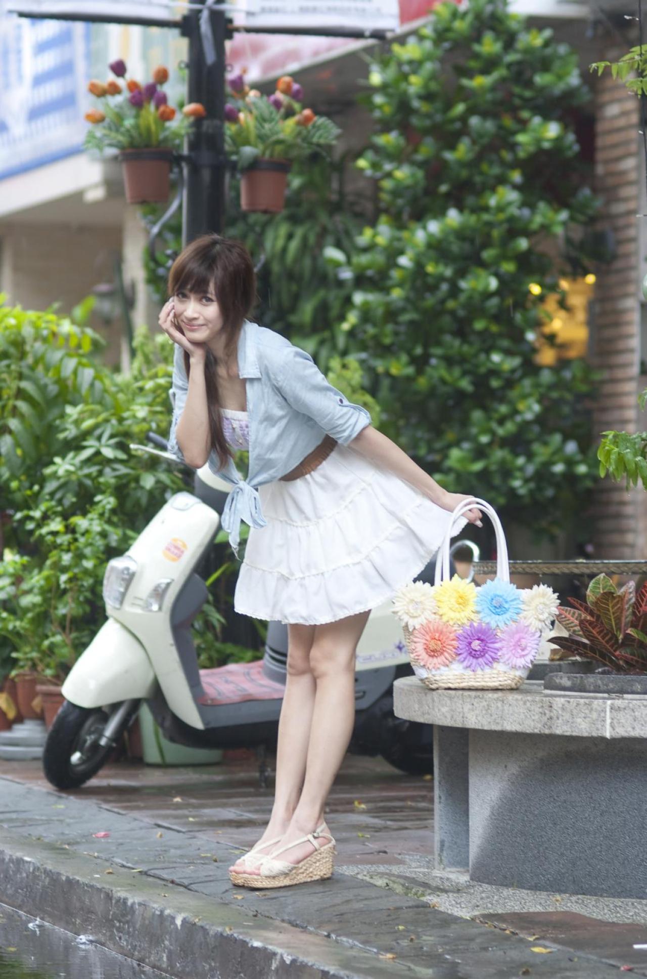 璟儿左手拎着花瓣装饰的挂包，右手撑着脸庞，略弯腰准备出发的姿势