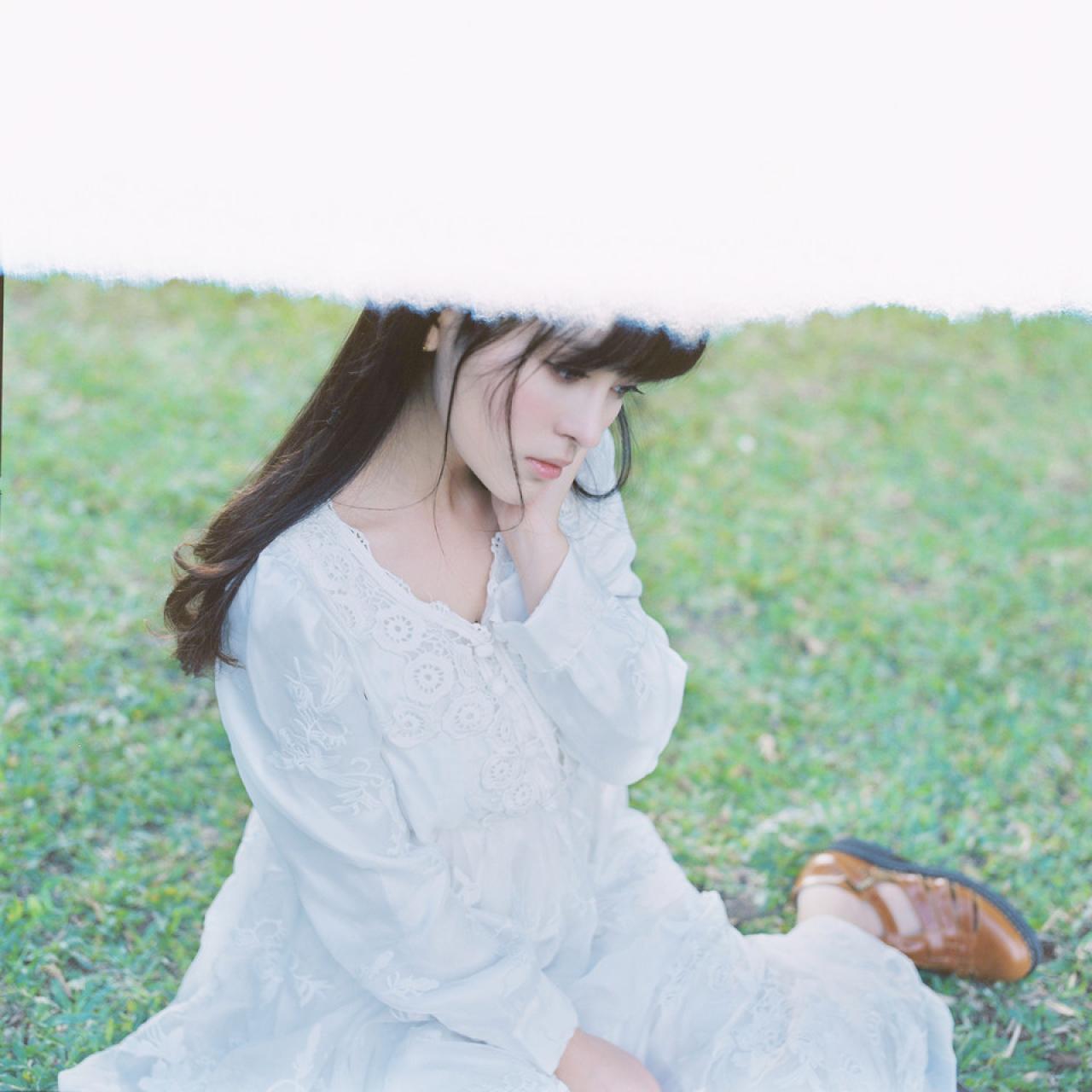 萌少女左手扶着脸颊，坐在草地上