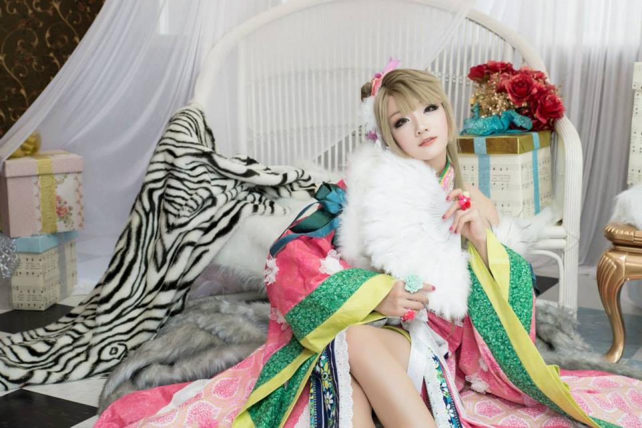 Miyuko扮演南小鸟坐在毯子上，靠在椅子上，双手扶扇