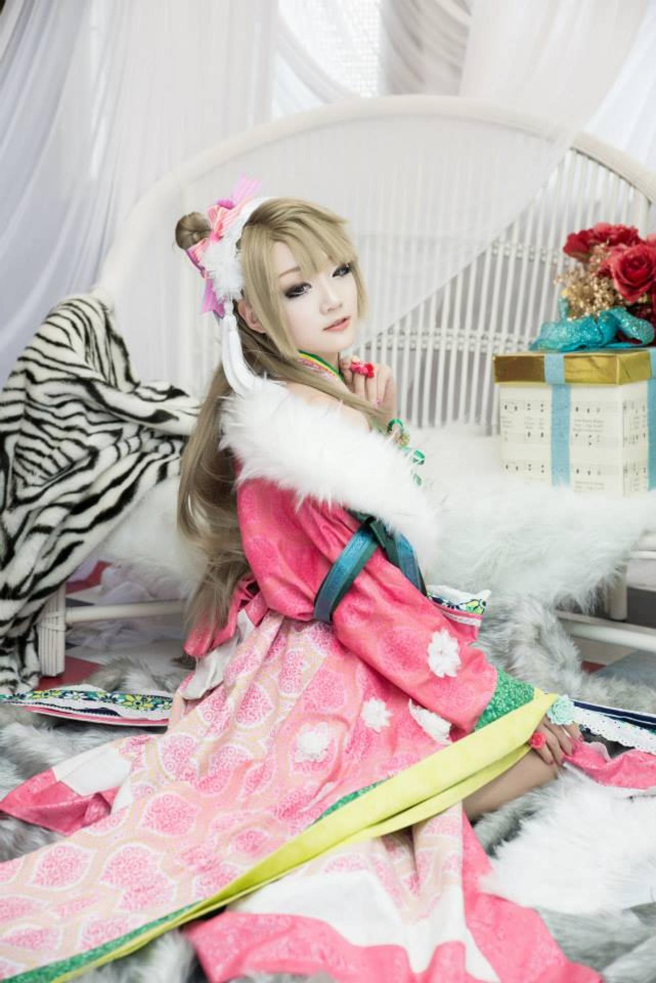 Miyuko扮演南小鸟跪坐在毯子上，左手贴着脖颈，右手搭在膝盖上