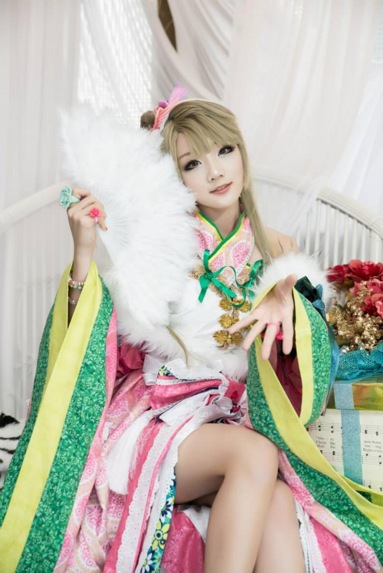 Miyuko扮演南小鸟右手持扇，左手五指伸开，坐在椅子上作邀请姿势