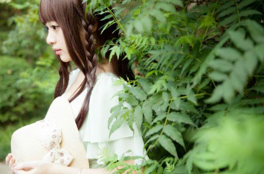 溢灯灯双手捧着帽子靠在绿叶之上的侧脸，麻花辫搭在肩膀