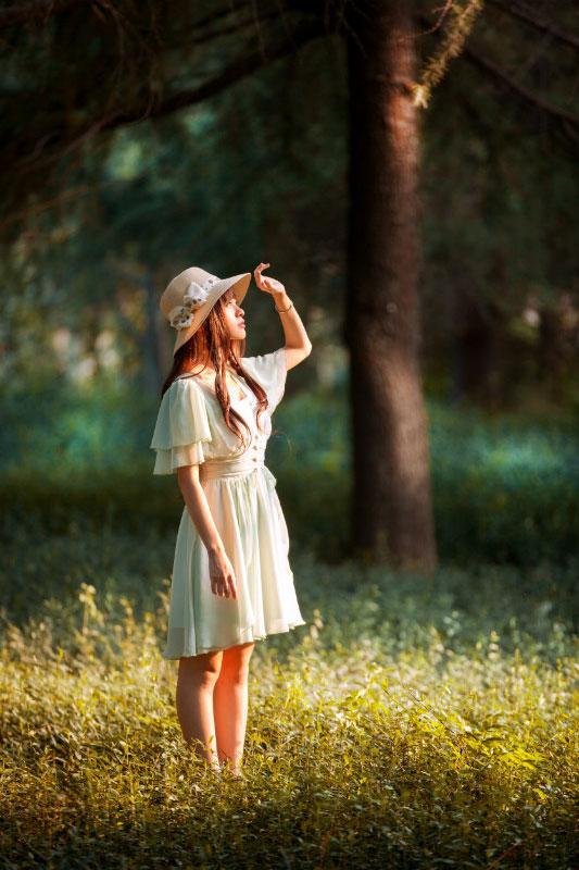 溢灯灯在树荫下，顺着太阳的方向，用手在额头前遮挡着阳光，仰望天空