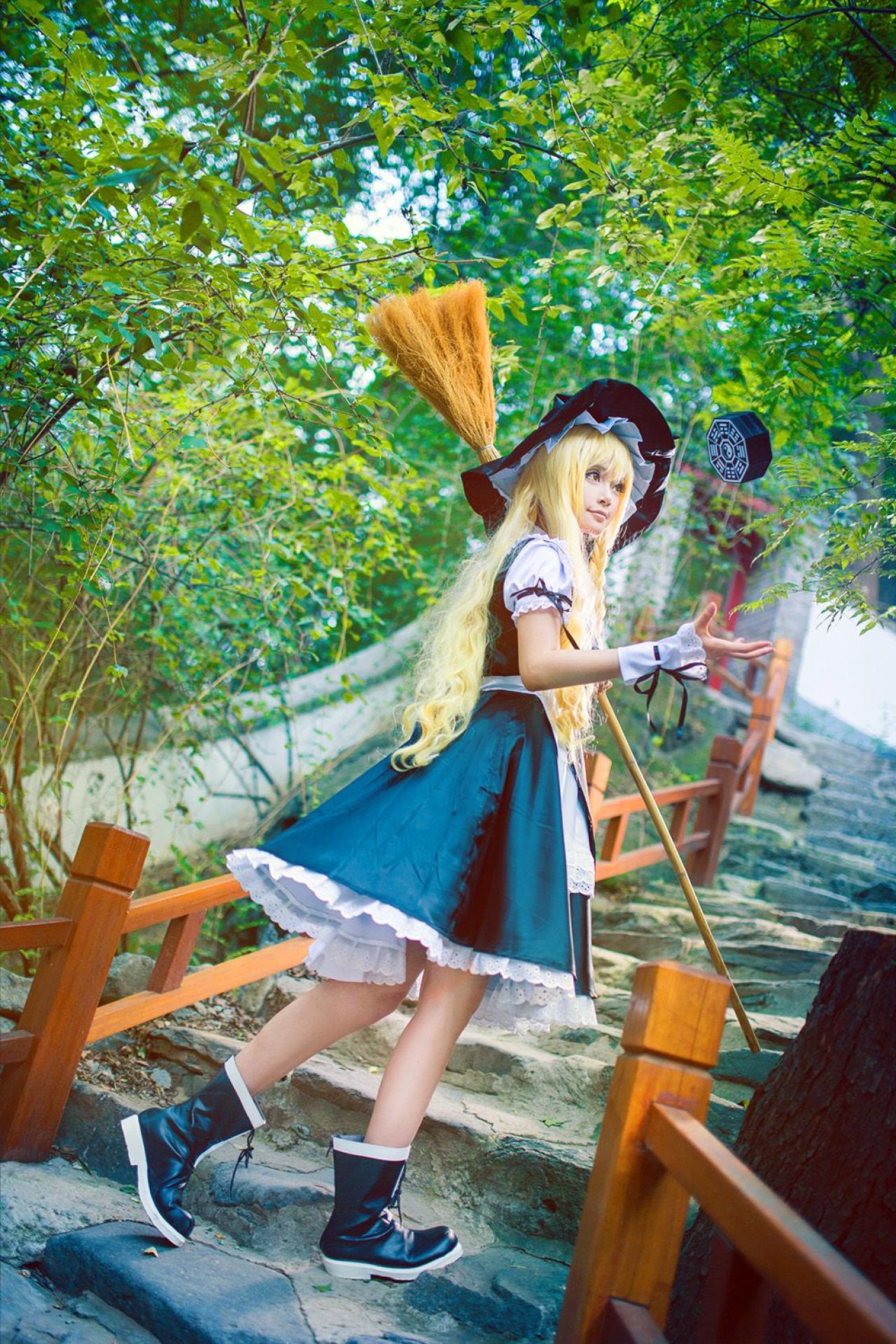 雨扮演雾雨魔理沙站在蜿蜒的石阶上，左臂扛着扫把，右手手掌将迷你八卦炉悬空捧起