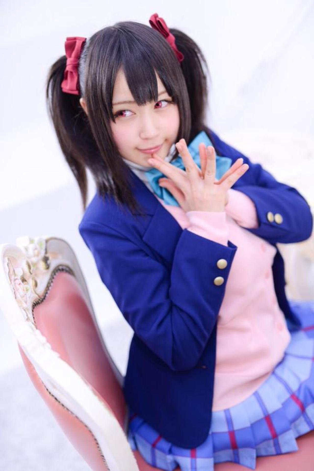 御伽ねこむ坐在椅子上，双手五指贴紧，侧目而视