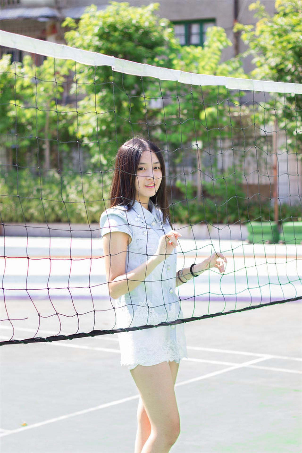 陈婕双手扒在球网后，微笑神情，立幅，侧面照