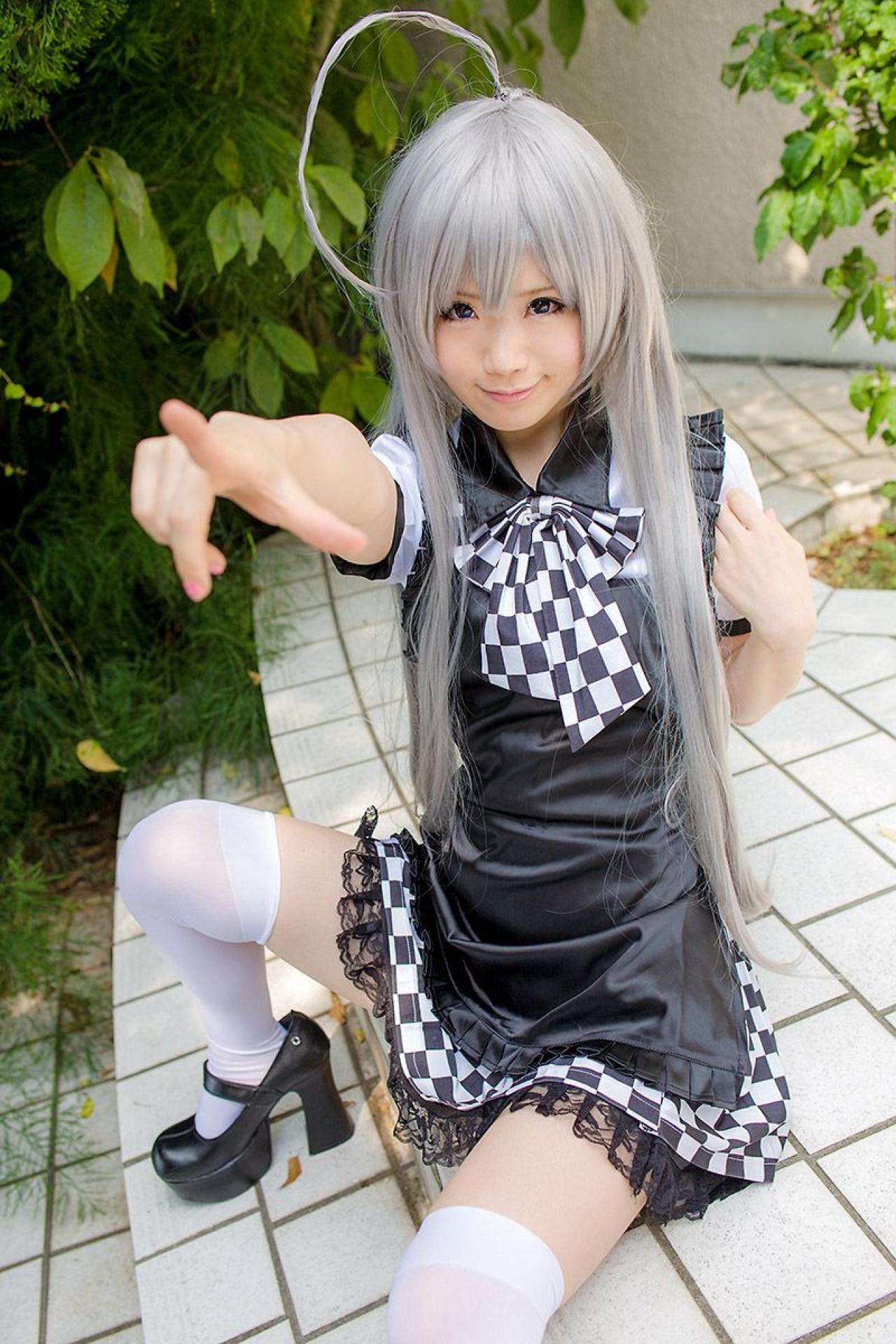 倉坂くるる坐在地上，左手放在肩部，伸出右臂，右手食指指向天空