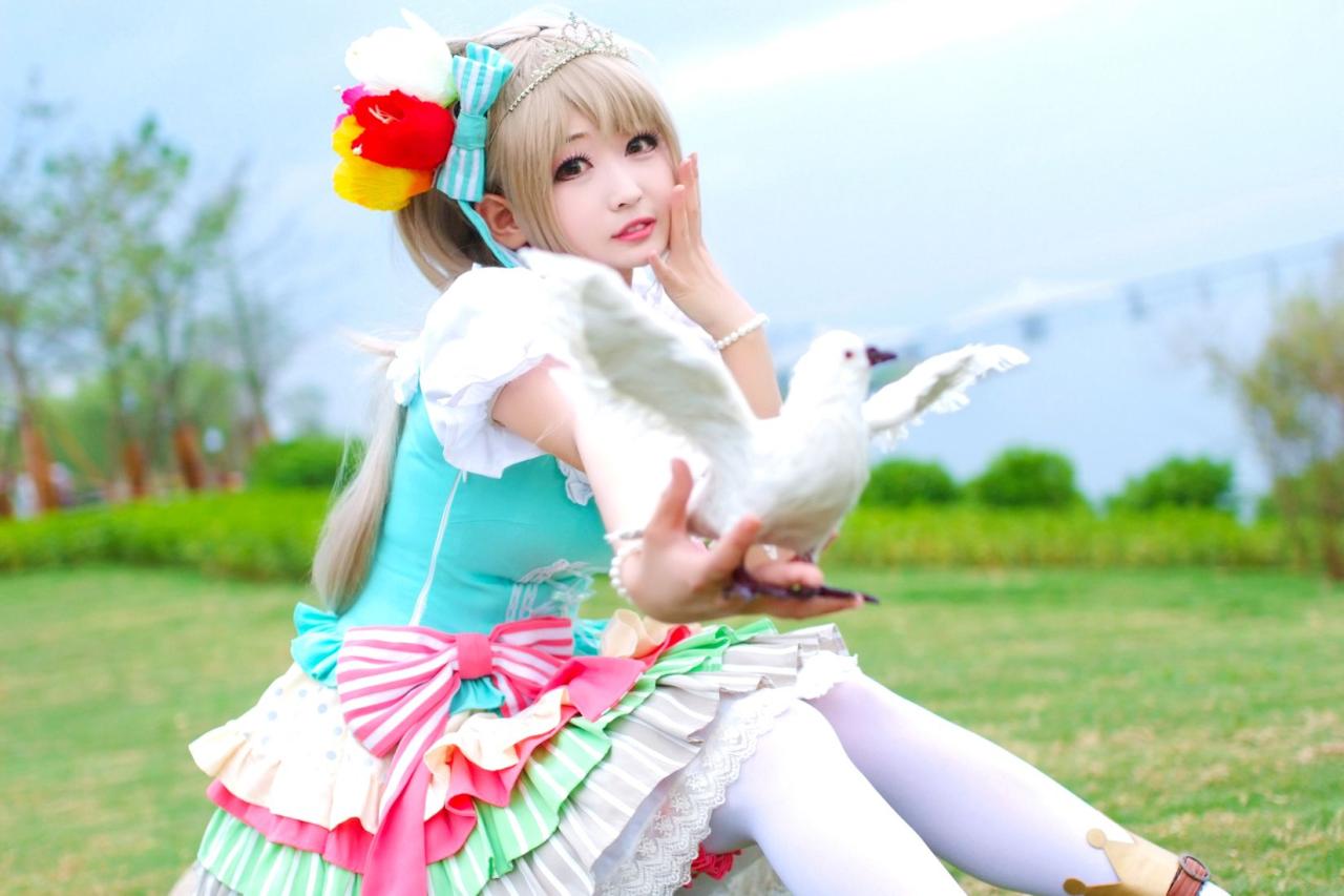 灼漪漪扮南小鸟坐在草地，左手扶脸，右手举着鸽子