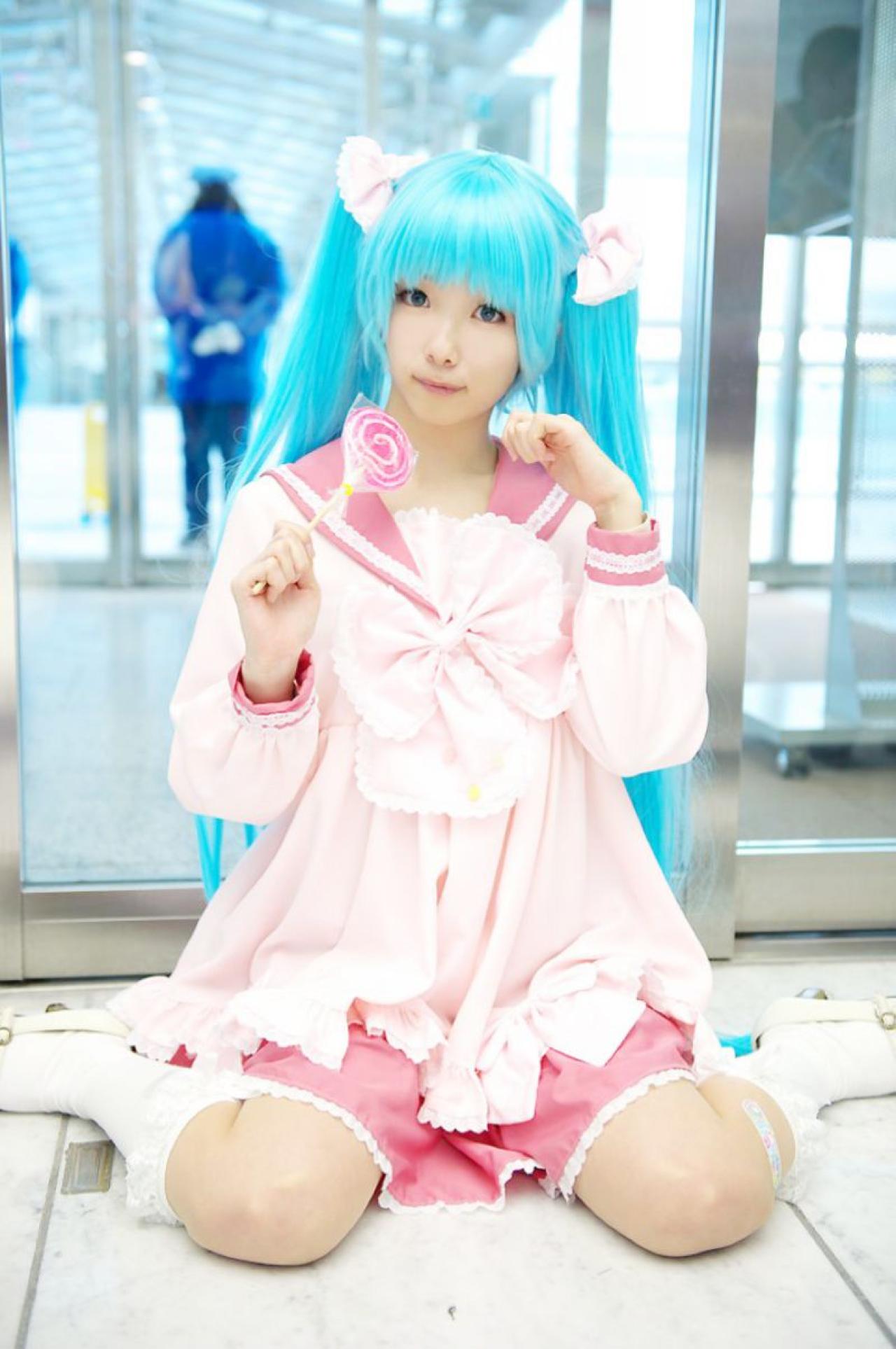 雪林檎扮初音未来跪坐在地上，右手拿着棒棒糖，左手半握拳