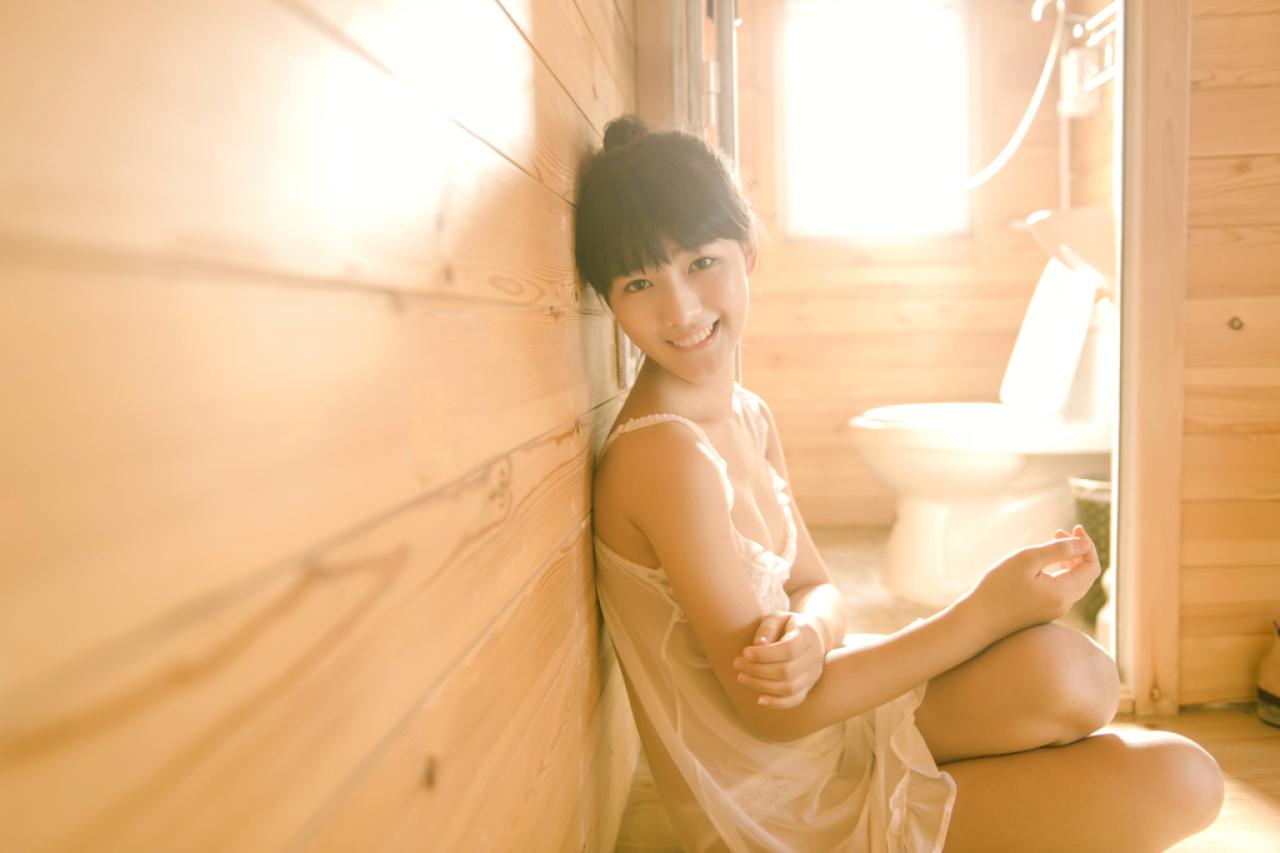 萌宅女侧身靠坐在木纹墙身上，扭过头微笑