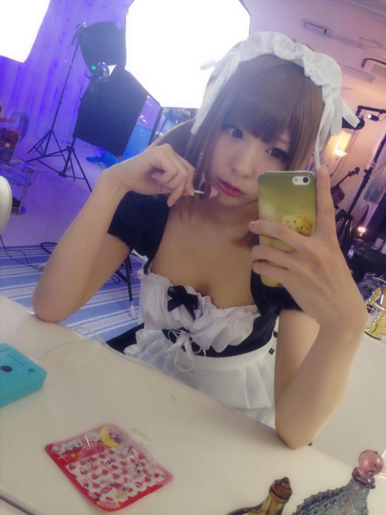 まゆふぁむ坐在圆桌前，右手拿着棒棒糖，看着左手拿着的手机