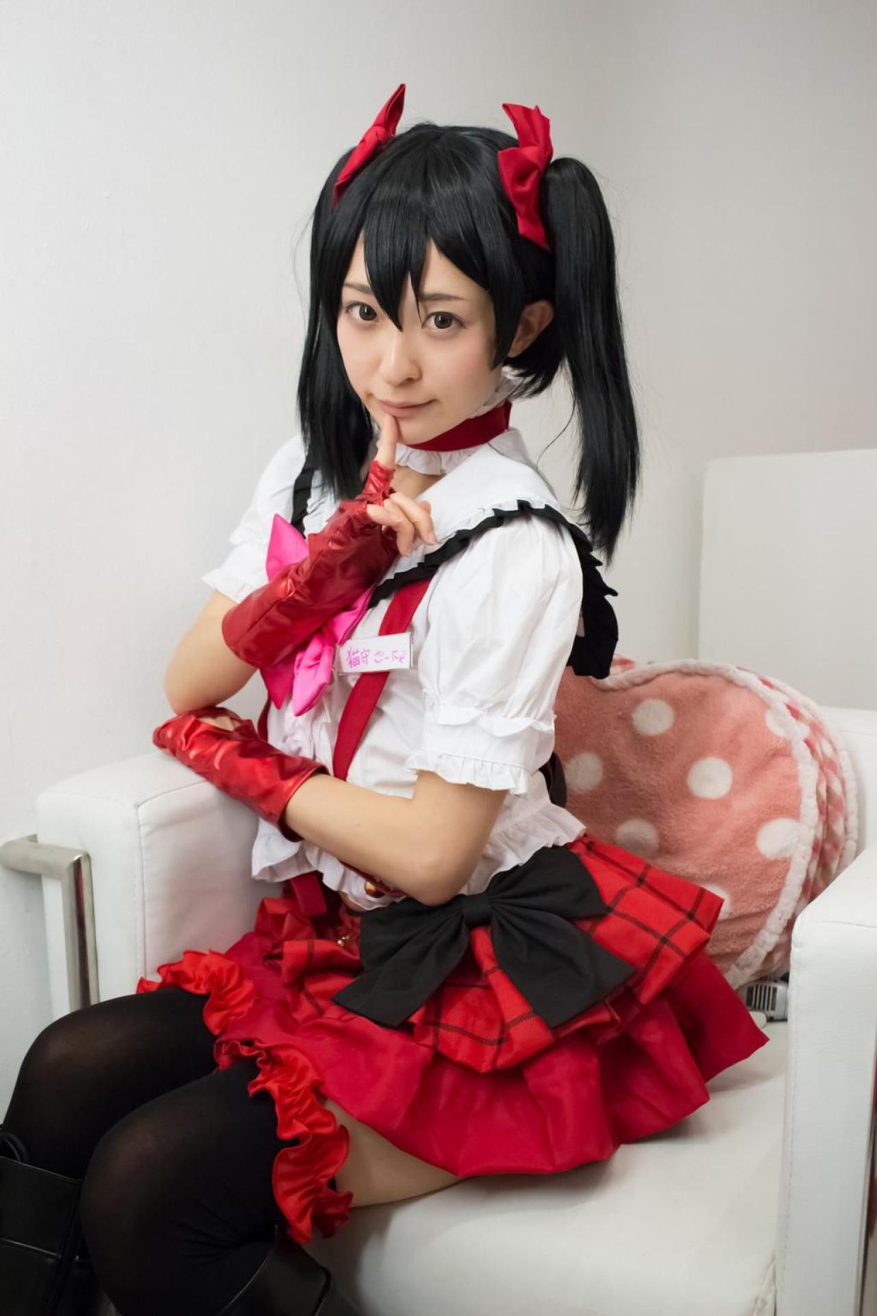 猫守ざーにゃ扮矢泽妮可坐在沙发，左手搭在沙发的扶手上，右手食指抵着下嘴唇