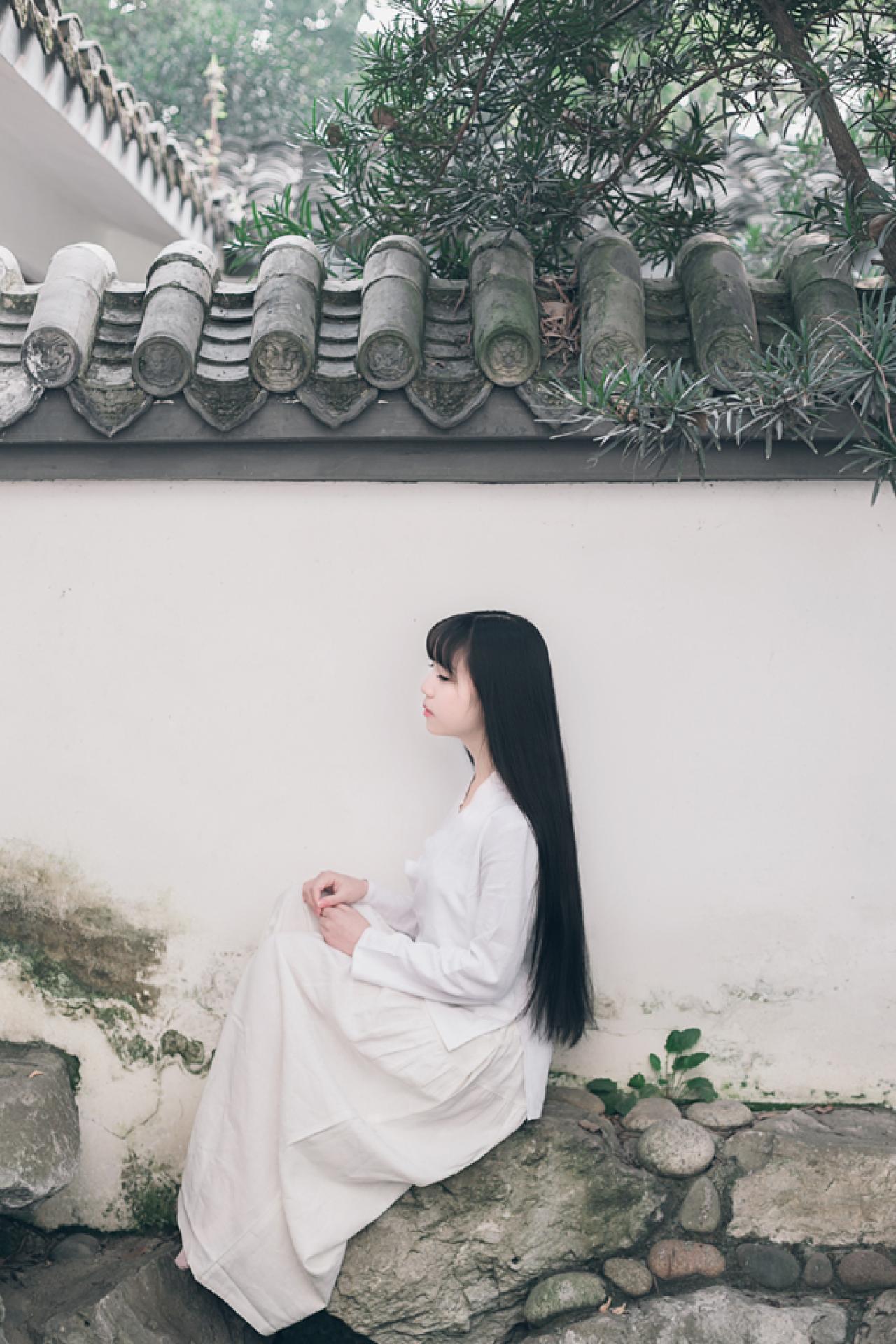 七七侧身坐在石头上，黑色长直发倾泻而下