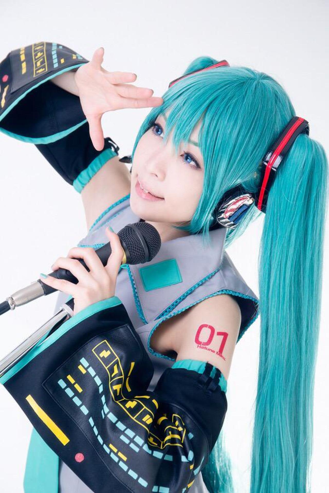 ろき扮初音未来左手拿着麦克风，右手遮挡灯光，抬头仰望 侧身照