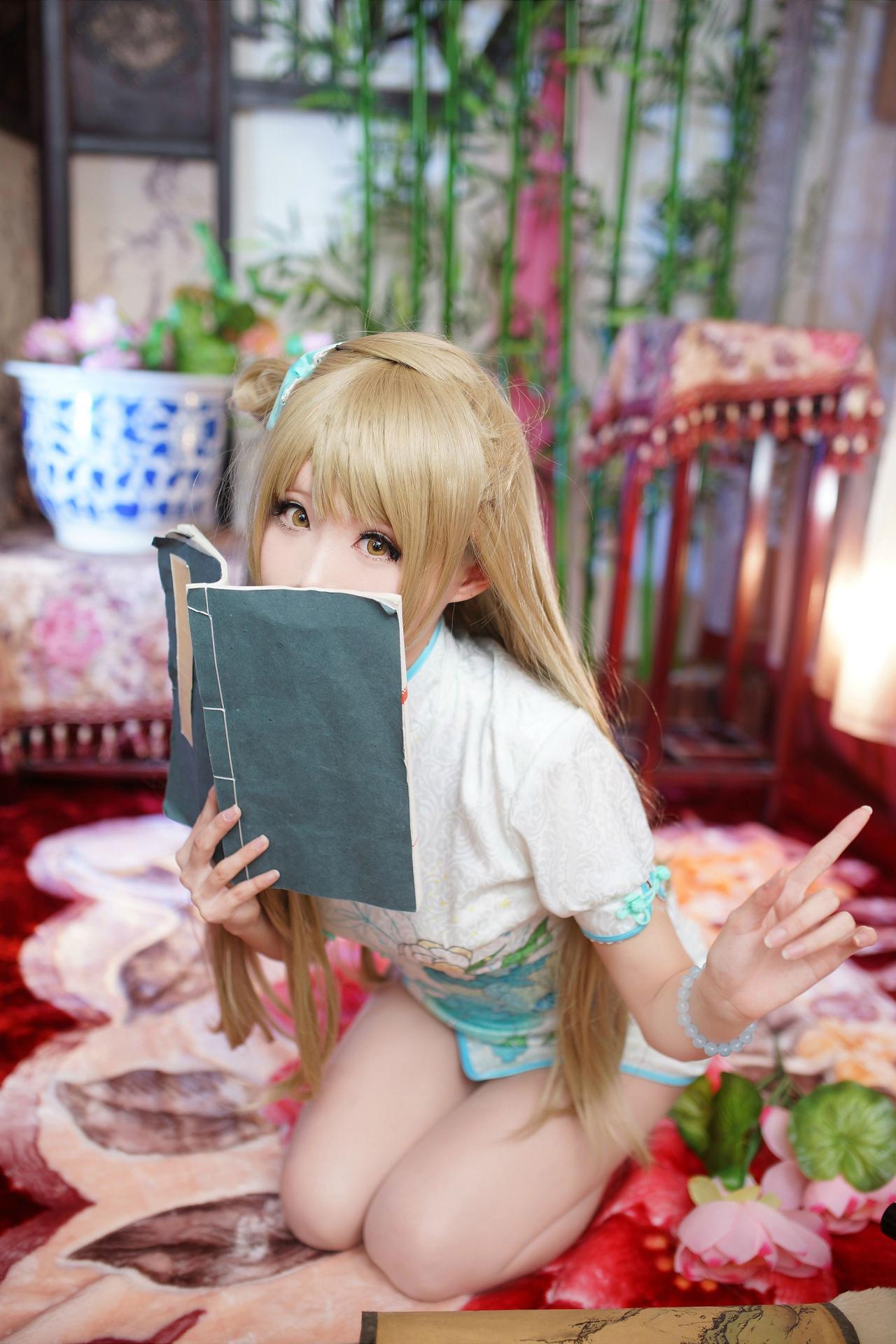 Meter扮南小鸟右手持扇遮面，左手竖起食指，跪坐在红色地毯上