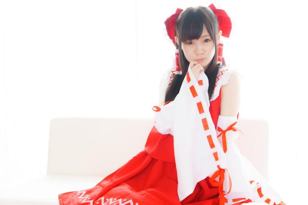 近衛りこ扮博丽灵梦跪坐在沙发上，抬起右手轻扶嘴角