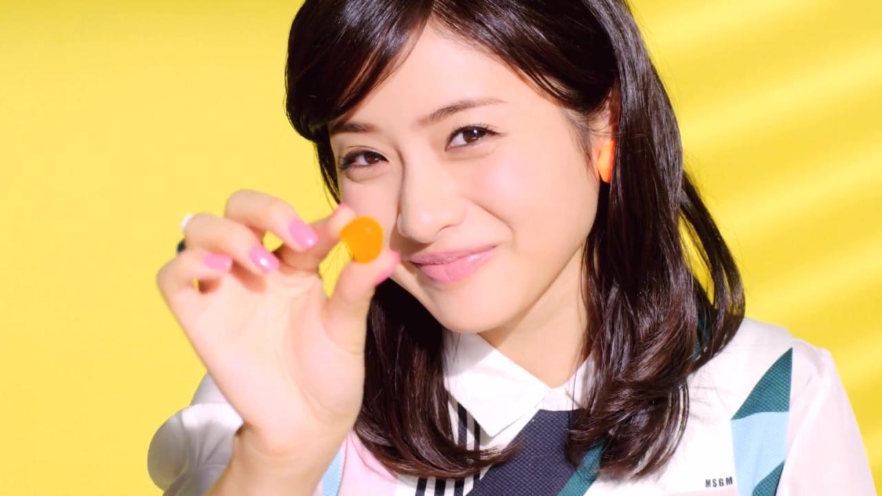 大拇指和食指捏着甜橙味果汁软糖送到嘴边的石原里美表情：啊，张嘴