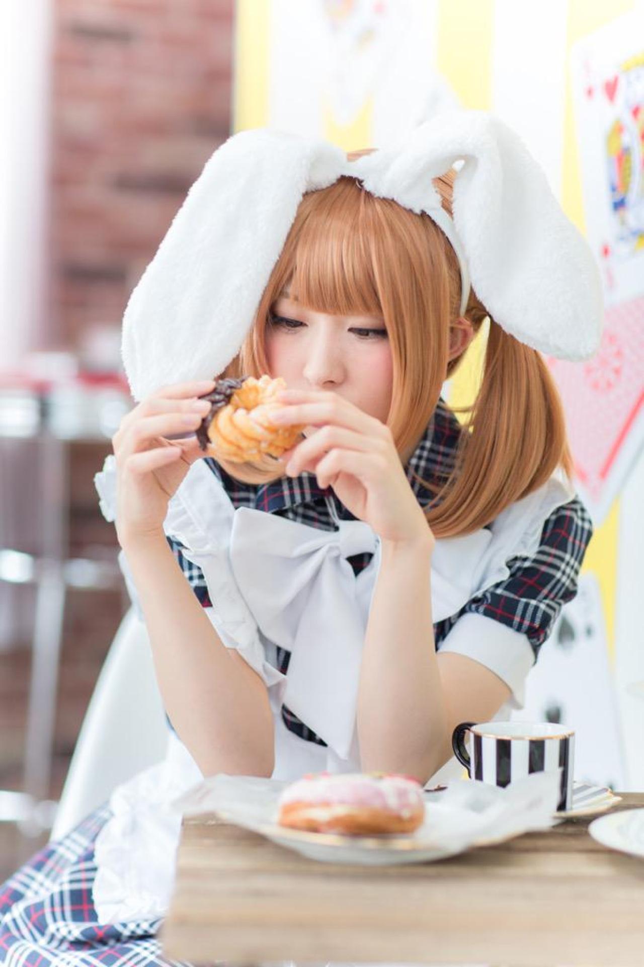 まゆふぁむ双手拿着面包圈，坐在桌旁，双手撑在桌子上