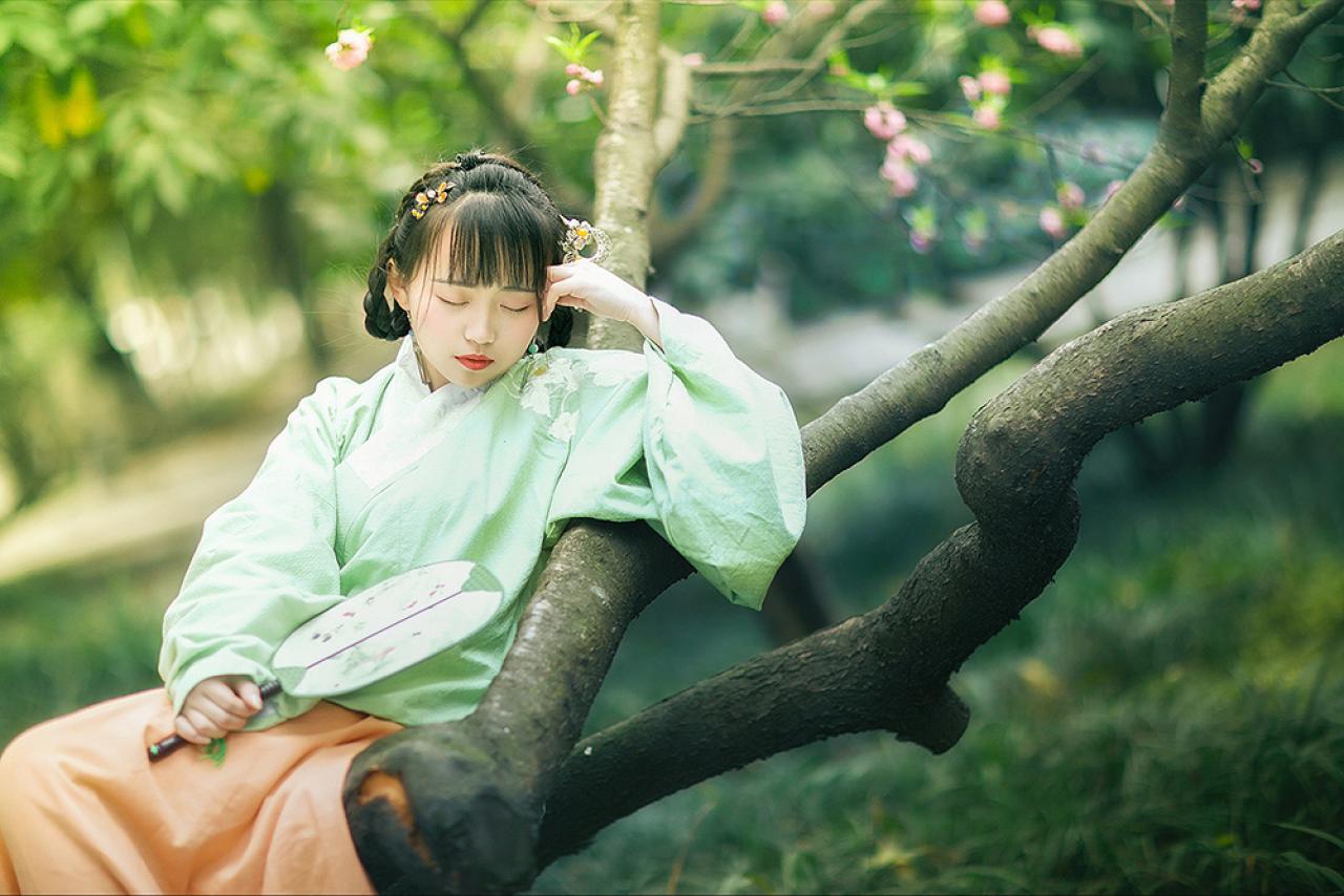 修老虎右手持扇依靠在梅花树干上，左手轻抵额头