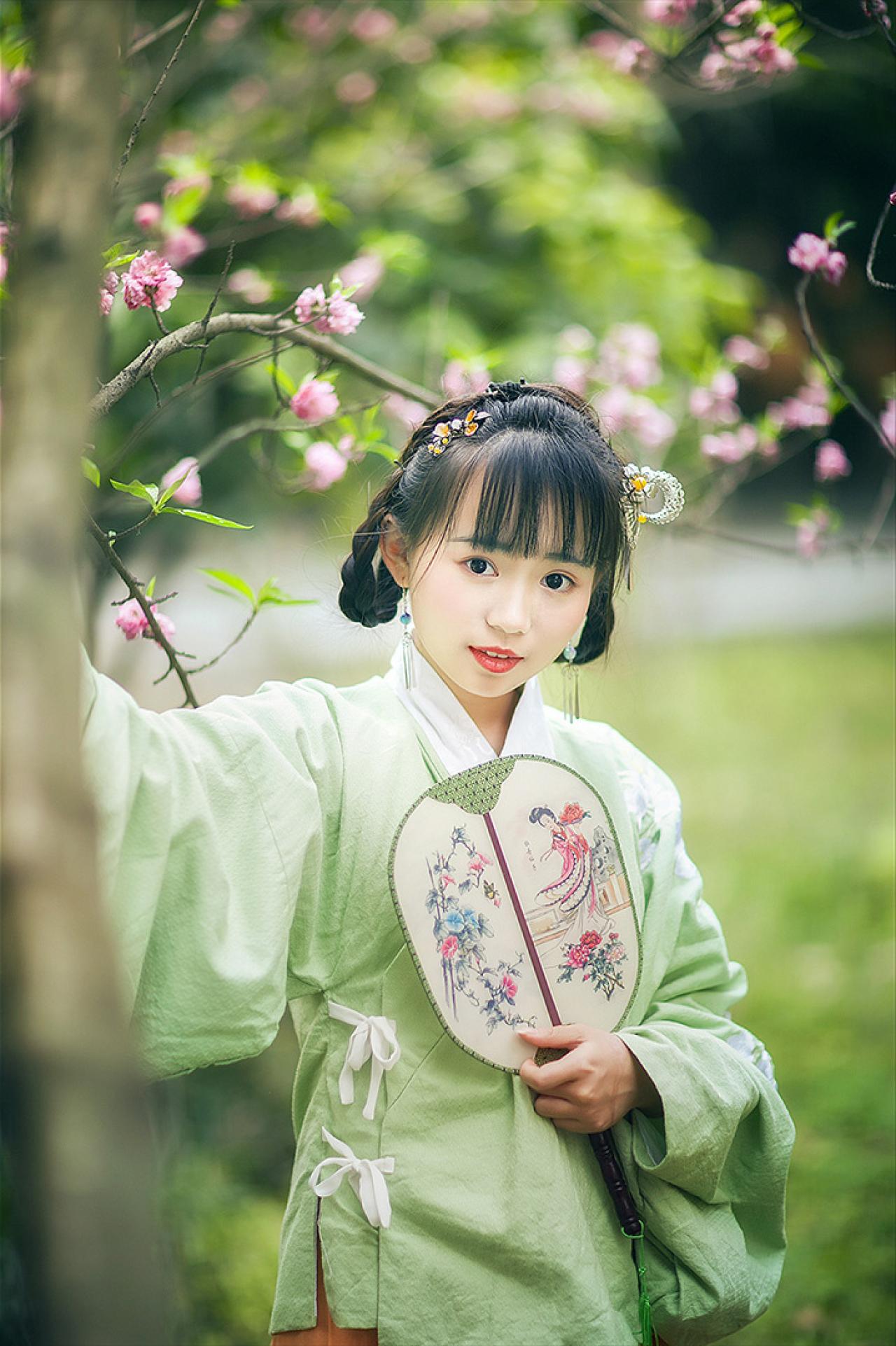 梅花枝下，修老虎左手持扇站在树旁，右手扶着树干