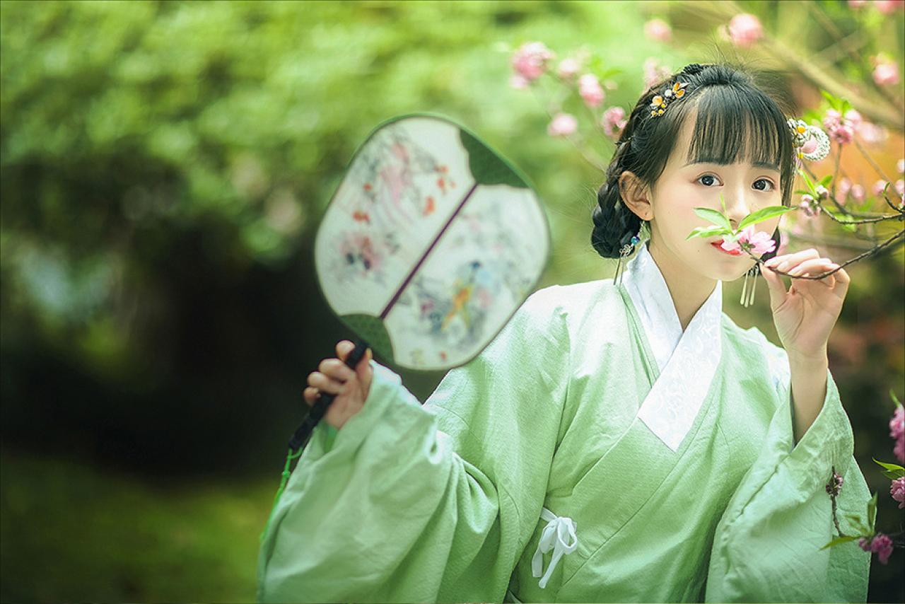 修老虎右手持扇，左手捏着梅花枝条，轻闻香气