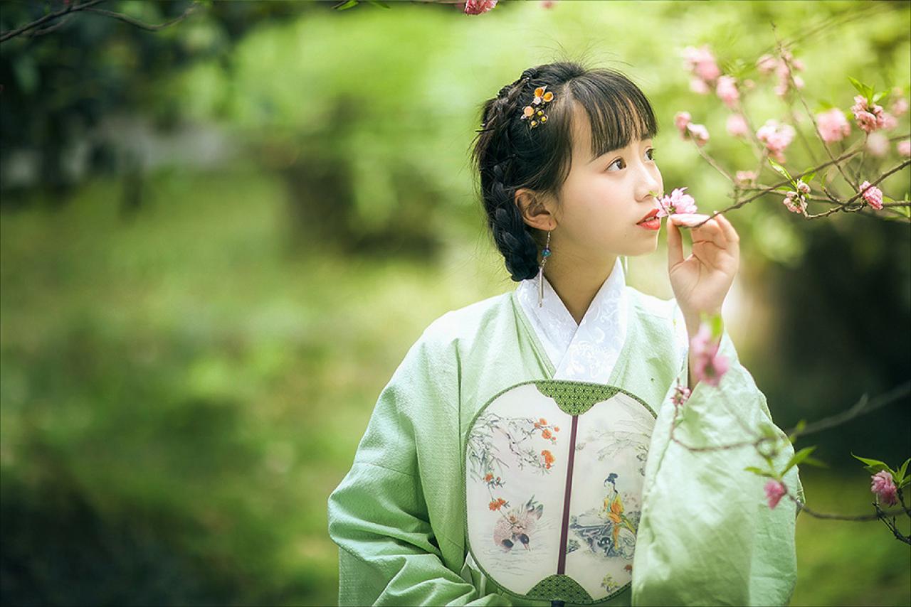 修老虎右手持扇放在怀中，侧目，左手捏着枝条，轻闻梅花