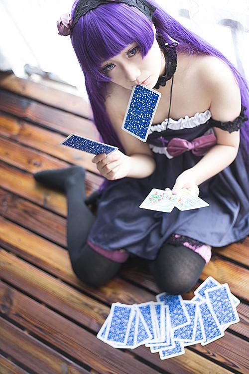 萌妹扮五更琉璃黑猫左手拿着两张塔罗牌，右手捏着一张，嘴里叼着一张塔罗牌，跪在地板上