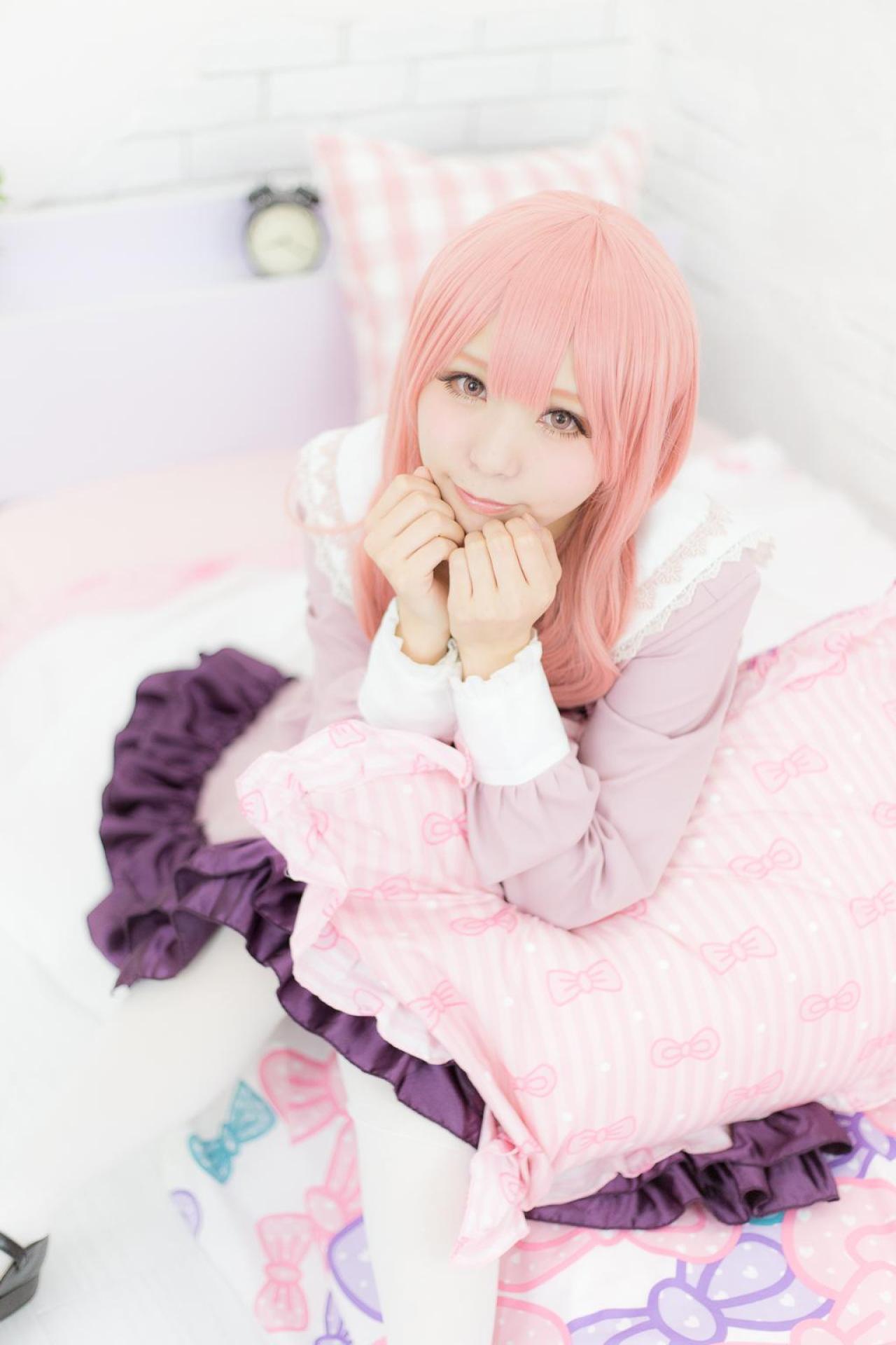 茉夏扮袴田日向双手握拳扶着下巴，手臂夹着枕头坐在床上